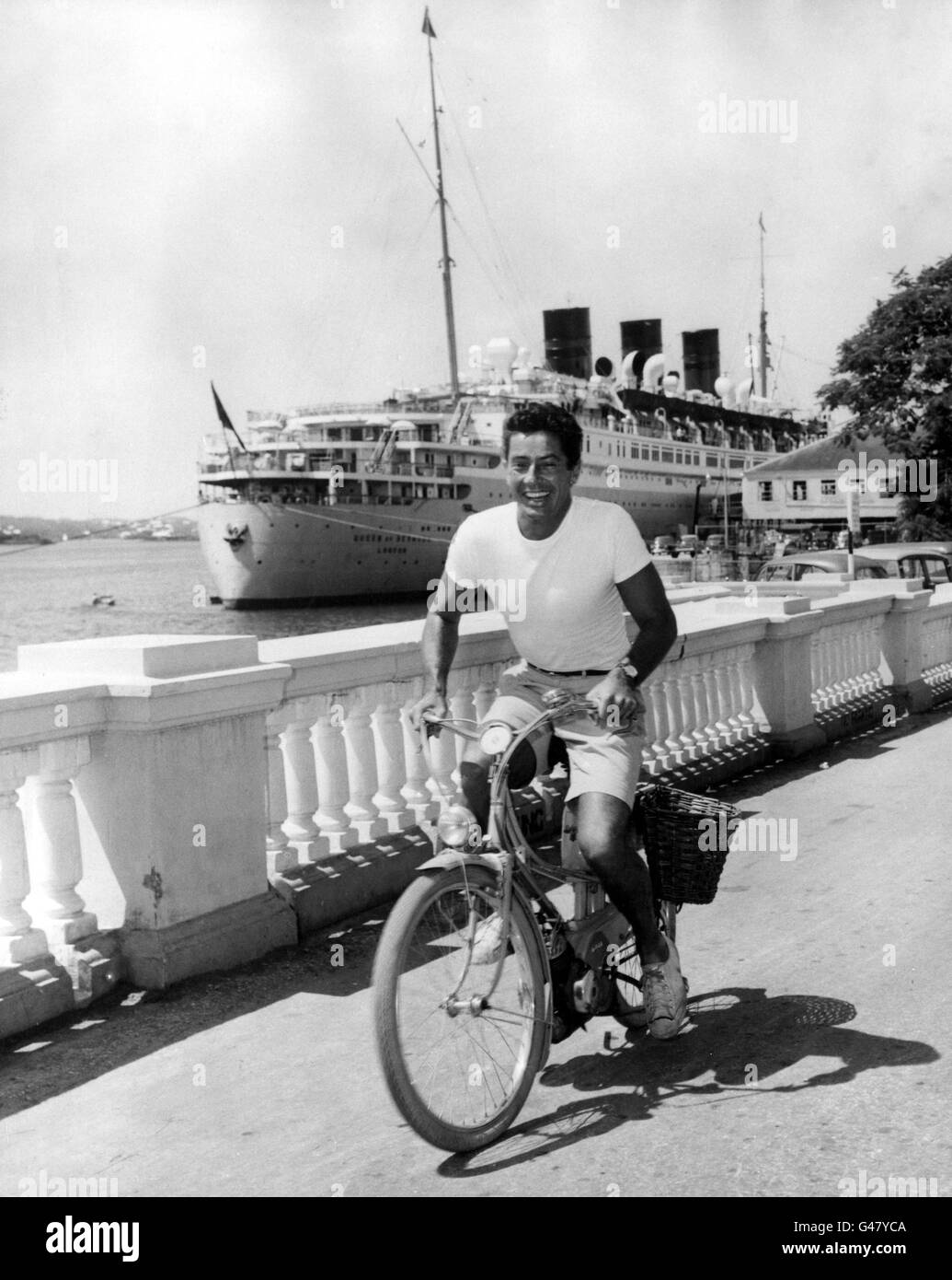 Hollywood-Schauspieler Farley Granger auf der Front Street, Hamilton, Bermuda, auf seinem motorgestützten Fahrrad. Im Hintergrund der Liner Queen of Bermuda. Zwischen Schauspielern machte der Star einen kurzen Urlaub in der Sonne der Insel. Stockfoto