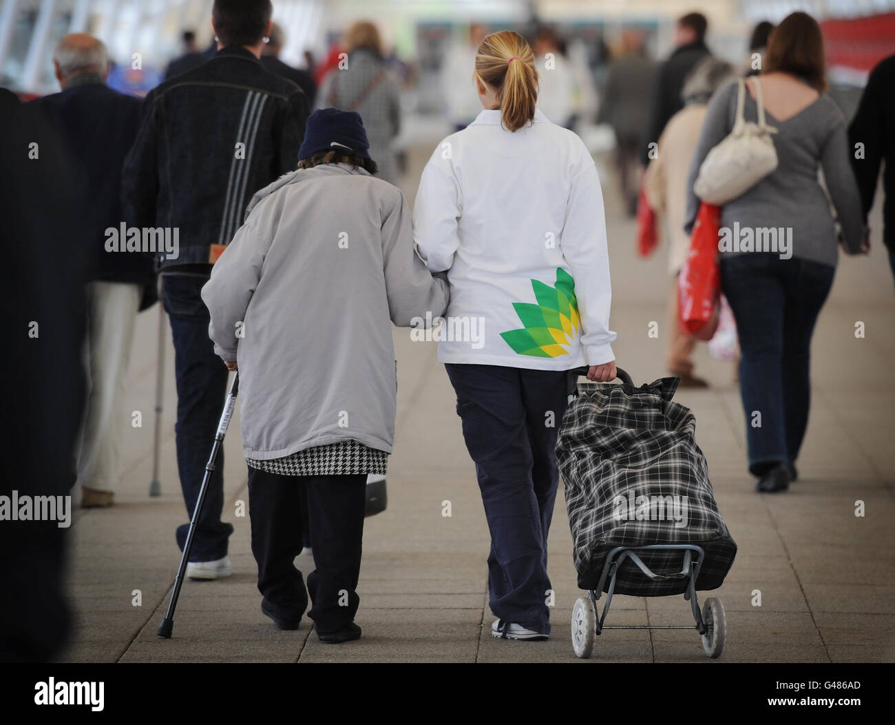 Eine Frau, die ein Sweatshirt mit einem BP-Logo (rechts) trägt, hilft einer Frau beim Verlassen der BP-Hauptversammlung im Excel-Zentrum in London. Stockfoto