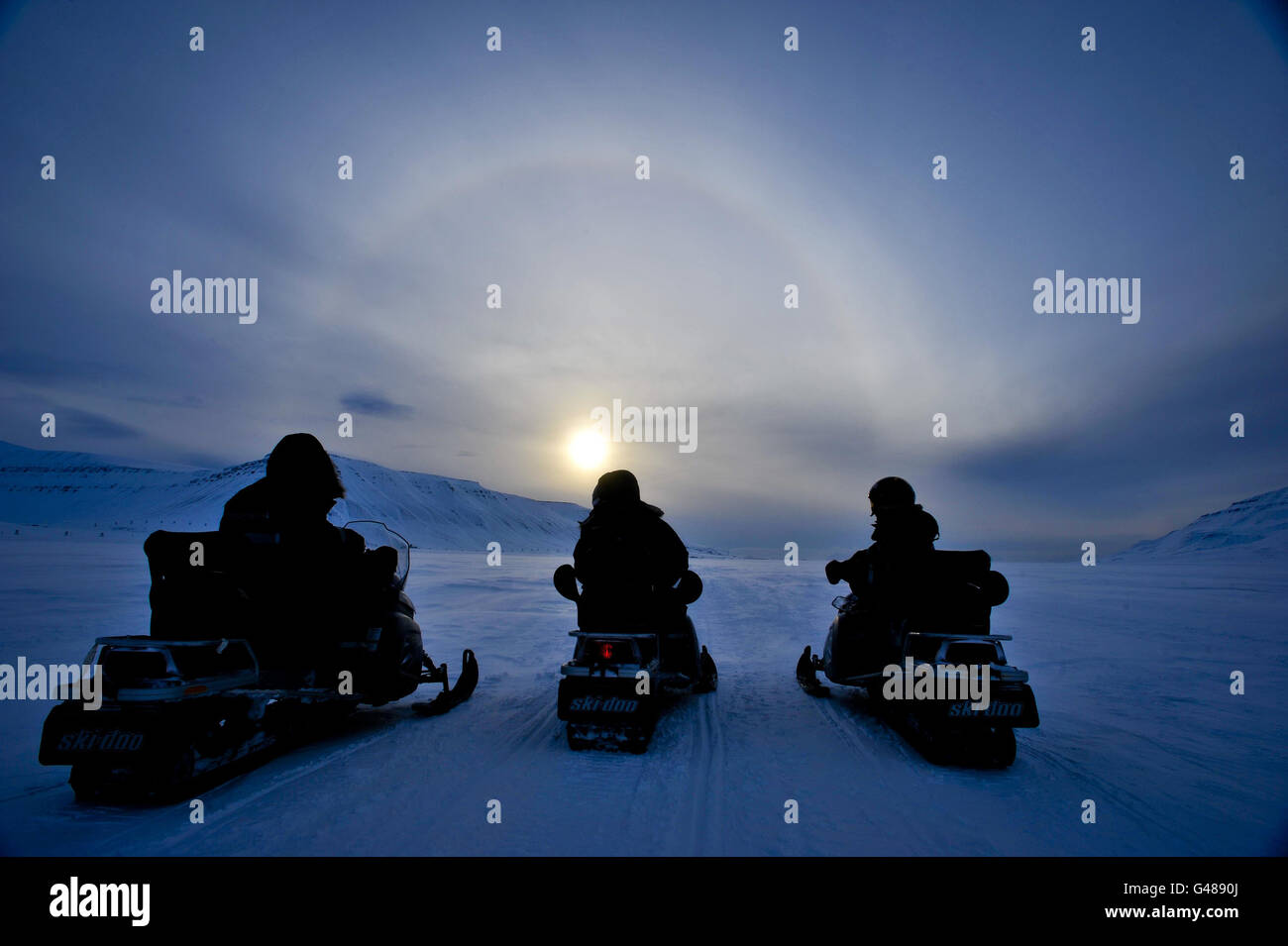 Die Leute auf den Ski-Doos bewundern einen Heiligenschein, auch bekannt als Nimbus, Eisbogen oder Gloriole, Das ist ein optisches Phänomen, das durch Eiskristalle in Zirruswolken hoch in der oberen Troposphäre auf der Insel Spitzbergen auf dem Spitzbergen-Archipel im Polarkreis entsteht, wenn die norwegischen Inseln in die Sommersonnenzeit eintreten. Stockfoto