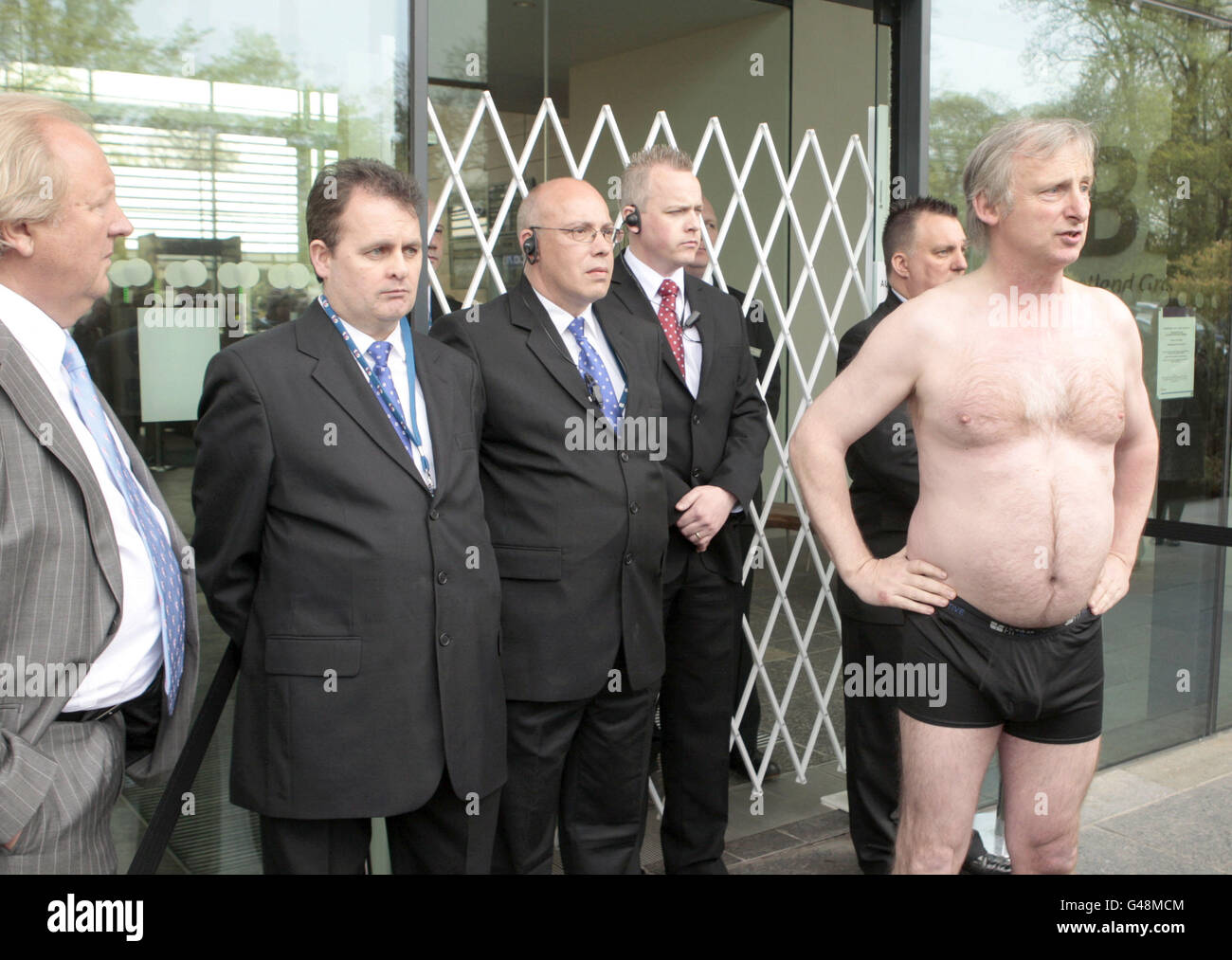 Der Protestierende Kit Fraser wird von der Sicherheitskontrolle beobachtet, nachdem er seine Kleidung vor der Generalversammlung der Royal Bank of Scotland in Edinburgh auszieht. Stockfoto