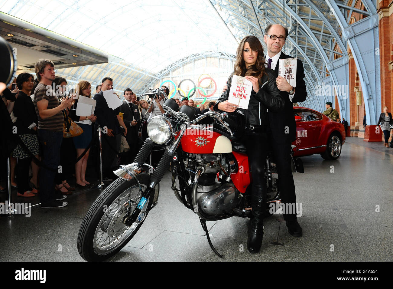 Der Thriller Jeffery Deaver kommt mit einem Bond-Mädchen an, um seinen neuen James-Bond-Roman "Carte Blanche" während einer Fotozelle am Bahnhof St. Pancras in London zu promoten. Stockfoto