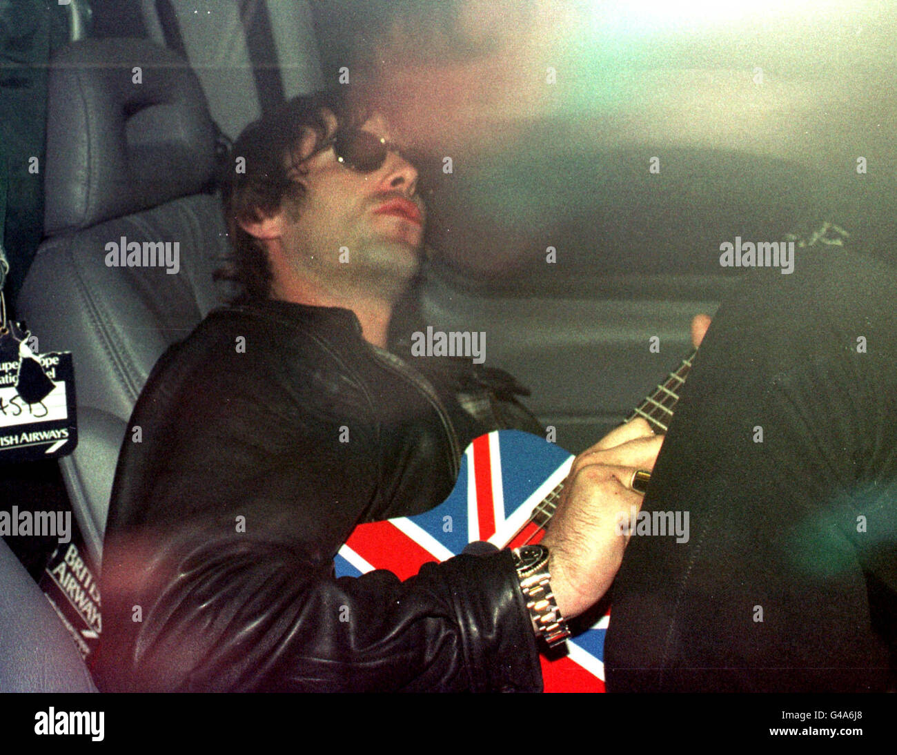 Liam Gallagher, Leadsänger der Rockband Oasis, klimpert auf seiner Gitarre, während er in abgedunkelten Limosinen vom Flughafen Gatwick vertrieben wird, nachdem er heute (Freitag) am Ende der weltweiten Tournee der Band aus Mexiko zurückgekehrt ist. Siehe PA Story SHOWBIZ Oasis. Foto von Adam Butler Stockfoto