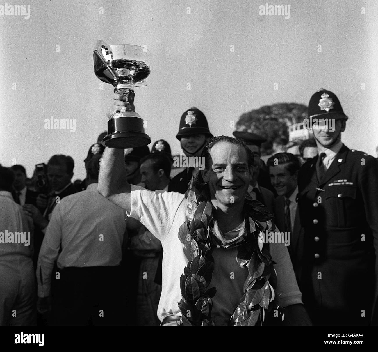 PA-NEWS FOTO-19.08.62: TRÄGT DER SIEGER LORBEEREN INNES IRELAND HÄLT DIE TASSE EMPOR NACH DEM GEWINN DER 27. RAC TOURIST TROPHY RENNEN AUF DEM GOODWOOD CIRCUIT. FAHREN EINES FERRARI BERLINETTA VON UDT/REASONABLY HE EINGEGEBEN 94,05 MEILEN IM DURCHSCHNITT EINE STUNDE FÜR DIE 100 RUNDEN (240 MEILEN) DES RENNENS, FINISHING 3.4. SEKUNDEN VOR GRAHAM HILL IN EINEM ÄHNLICHEN AUTO Stockfoto