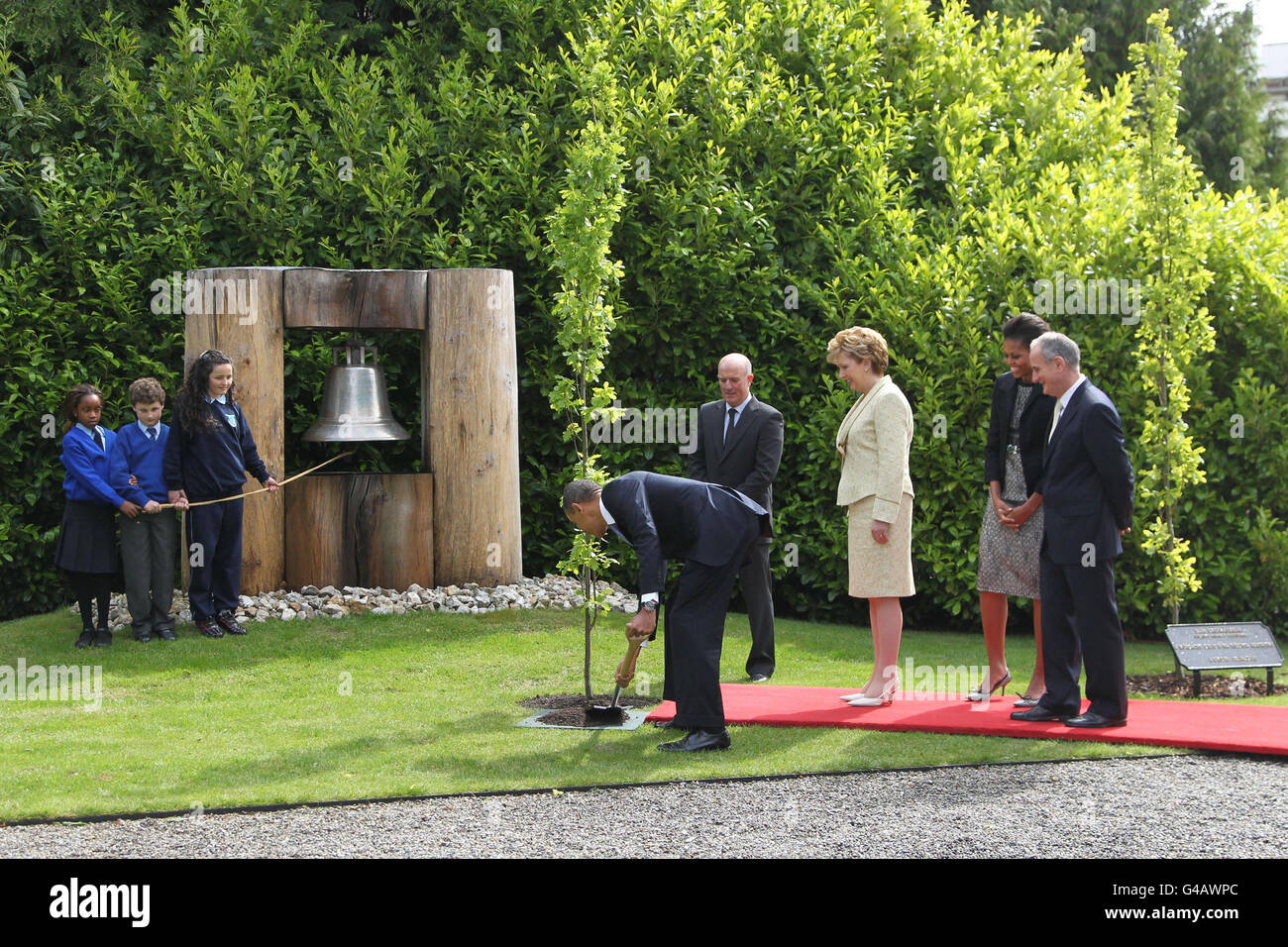 Schulkinder, Onyedita Ukachukwu 8, Colm Dunne 9 und Margaret McDonagh 10 stehen bei der Friedensglocke als US-Präsident Barack Obama, Pflanzen einen Baum in Aras an Uachtarain, Phoenix Park, beobachtet von Robert Norris, Leiter Gärtner, irische Präsidentin Mary McAleese, Ihr Ehemann Dr. Martin McAleese (rechts) und First Lady Michelle Obama während des Besuchs von Präsident Obama in Irland. Stockfoto