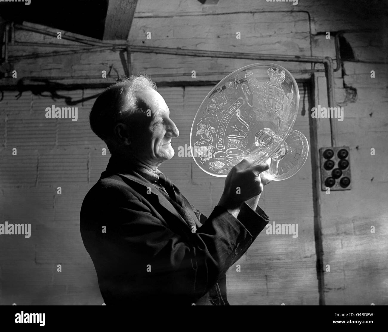 F.C Shotton untersucht ein Stück Krönungsglas, Produkt von Handwerkern in Stourbridge, Worcestershire. Die Schale trägt das königliche Wappen und die Inschrift: Lang darf sie regieren. Stockfoto