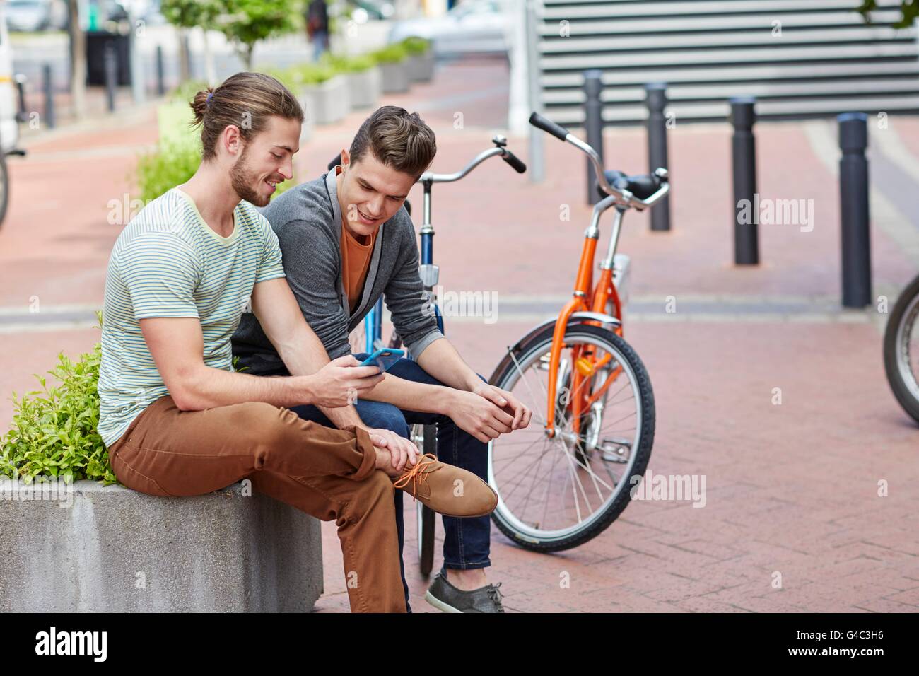 -MODELL VERÖFFENTLICHT. Zwei junge Männer sitzen auf Wand mit Smartphone. Stockfoto