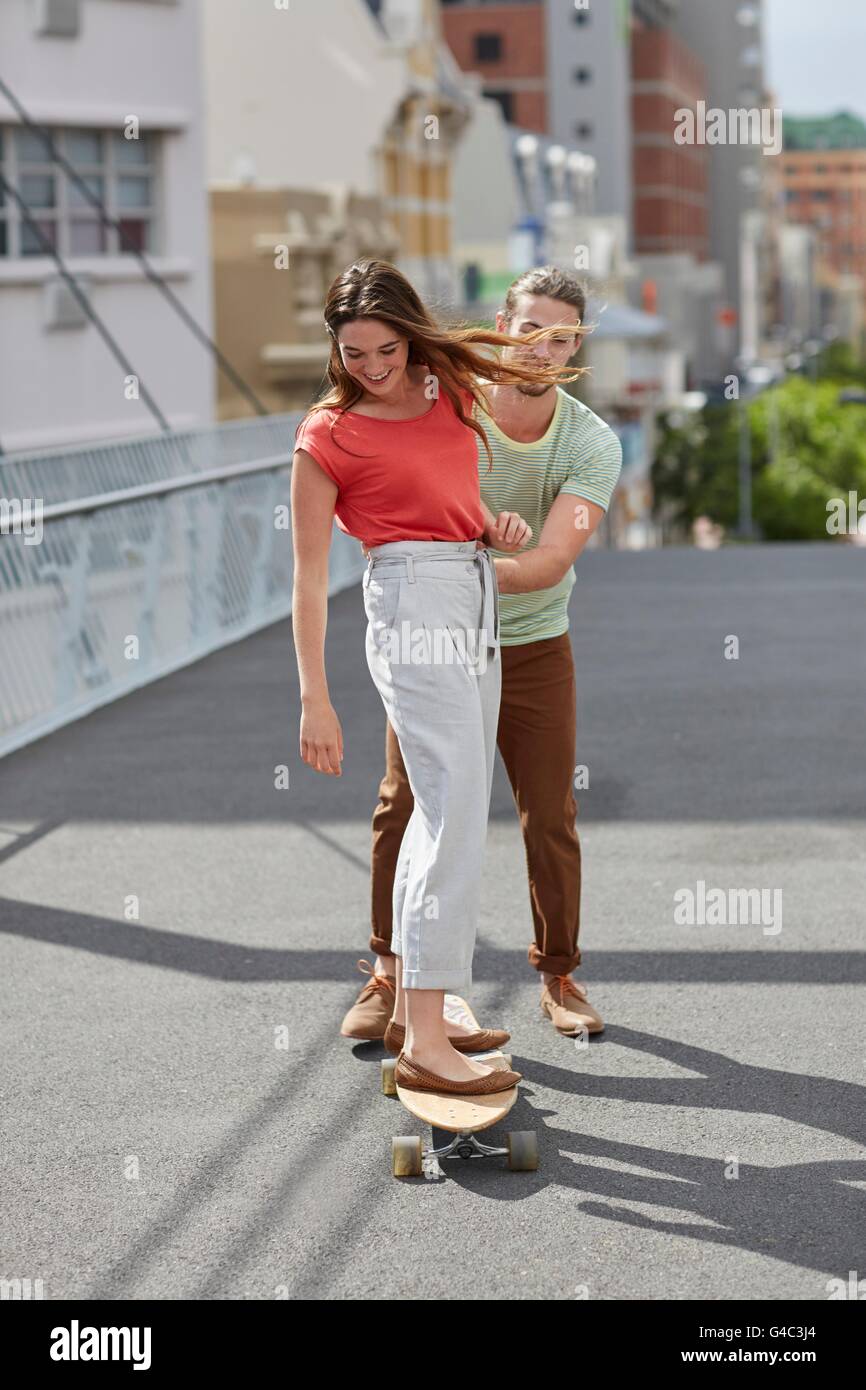 -MODELL VERÖFFENTLICHT. Junge Frau mit Mann schob skateboarding. Stockfoto