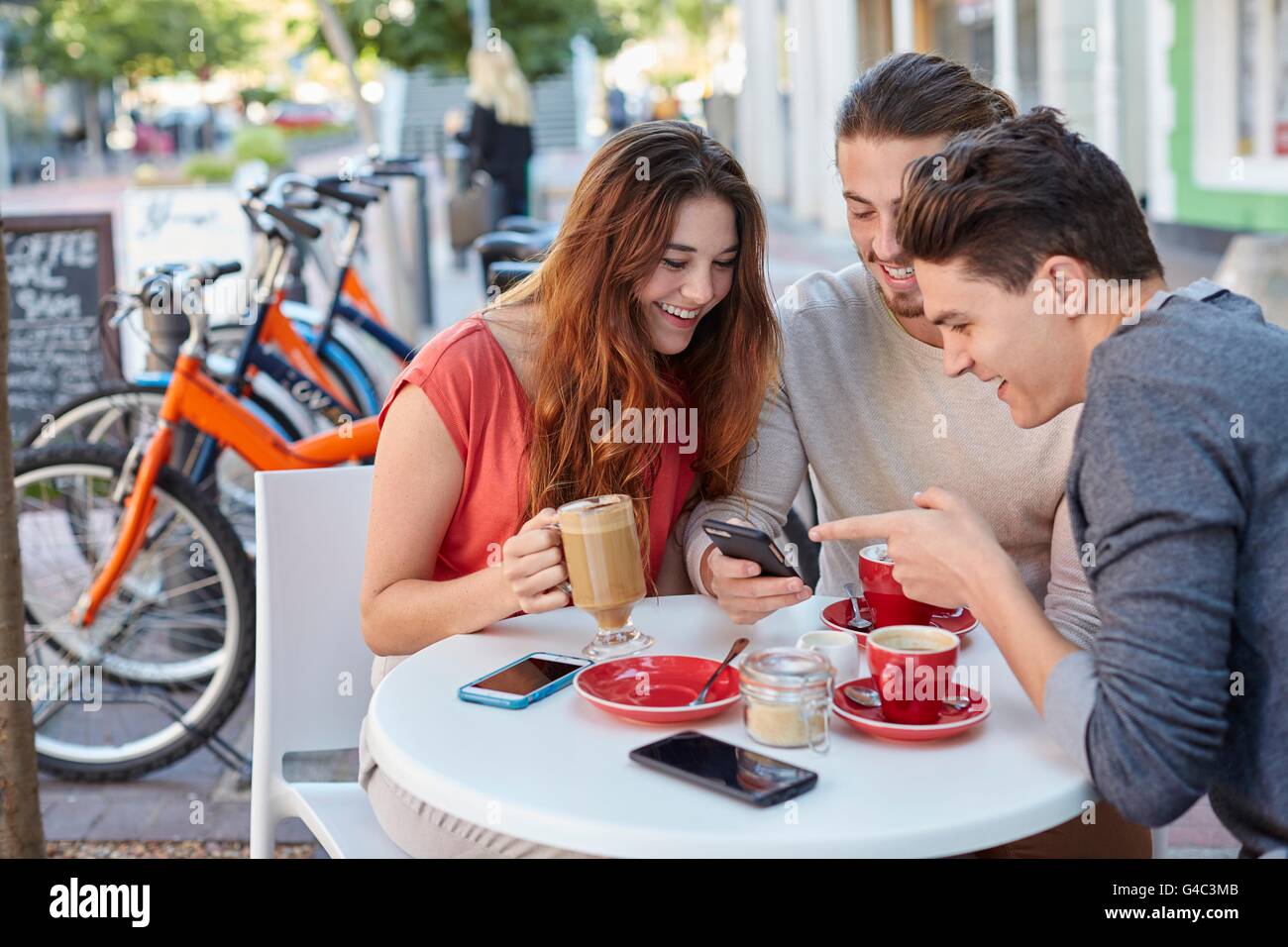 -MODELL VERÖFFENTLICHT. Drei jungen Freunden im Café mit Smartphone. Stockfoto