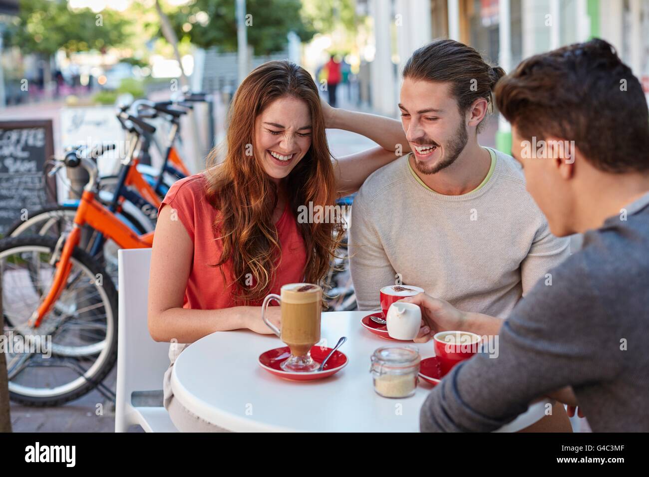 -MODELL VERÖFFENTLICHT. Drei jungen Freunden im Café mit heißen Getränken, lächelnd. Stockfoto