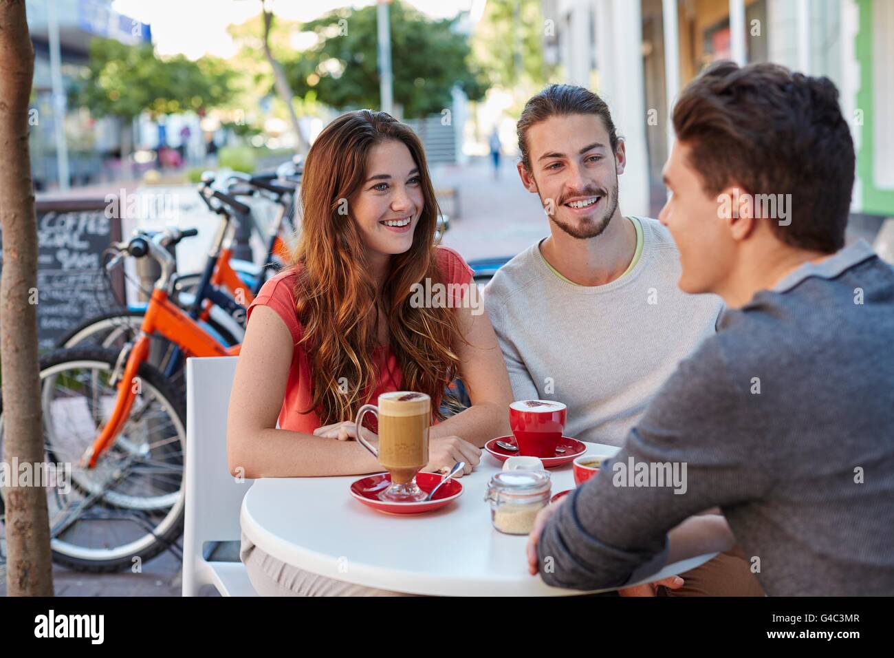 -MODELL VERÖFFENTLICHT. Drei jungen Freunden im Café mit heißen Getränken, lächelnd. Stockfoto