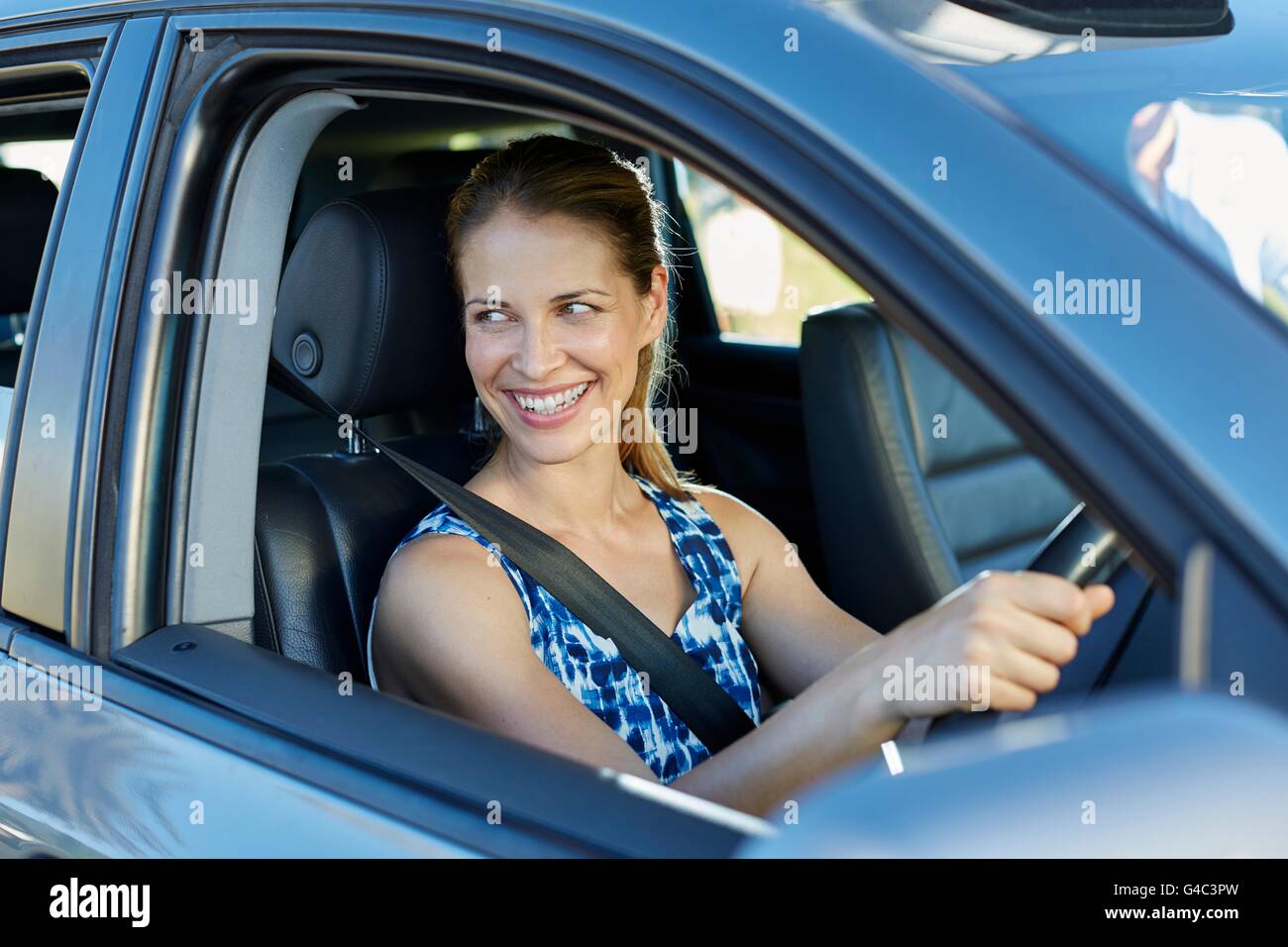 -MODELL VERÖFFENTLICHT. Junge Frau auf der Suche durch Autofenster, lächelnd. Stockfoto