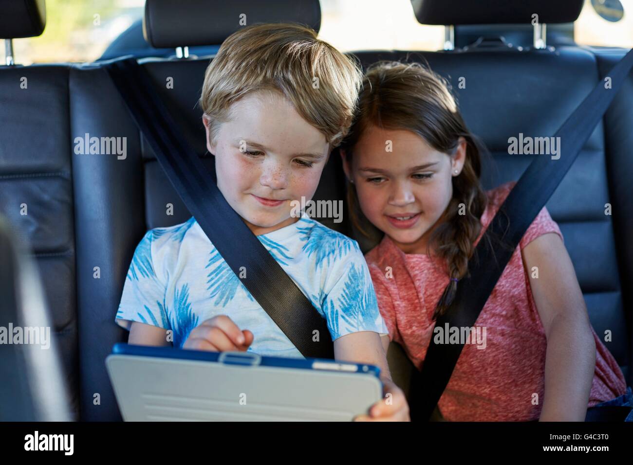-MODELL VERÖFFENTLICHT. Bruder und Schwester auf dem Rücksitz des Autos angeschnallt, mit einem digitalen Tablet. Stockfoto