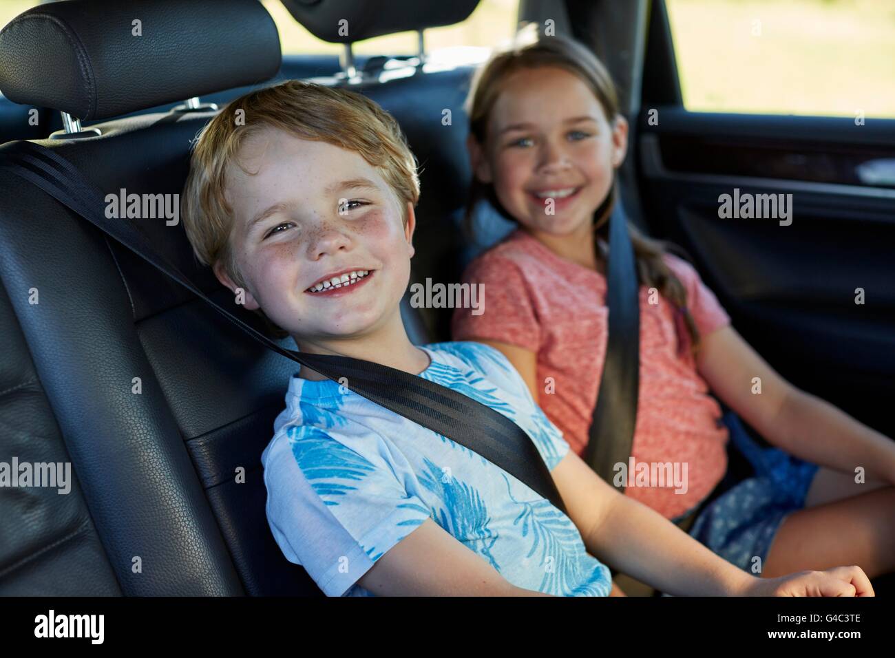 -MODELL VERÖFFENTLICHT. Bruder und Schwester auf dem Rücksitz des Autos angeschnallt. Stockfoto