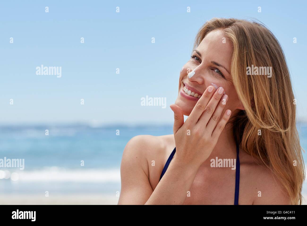 -MODELL VERÖFFENTLICHT. Junge Frau, die Anwendung von Sonnencreme am Strand. Stockfoto