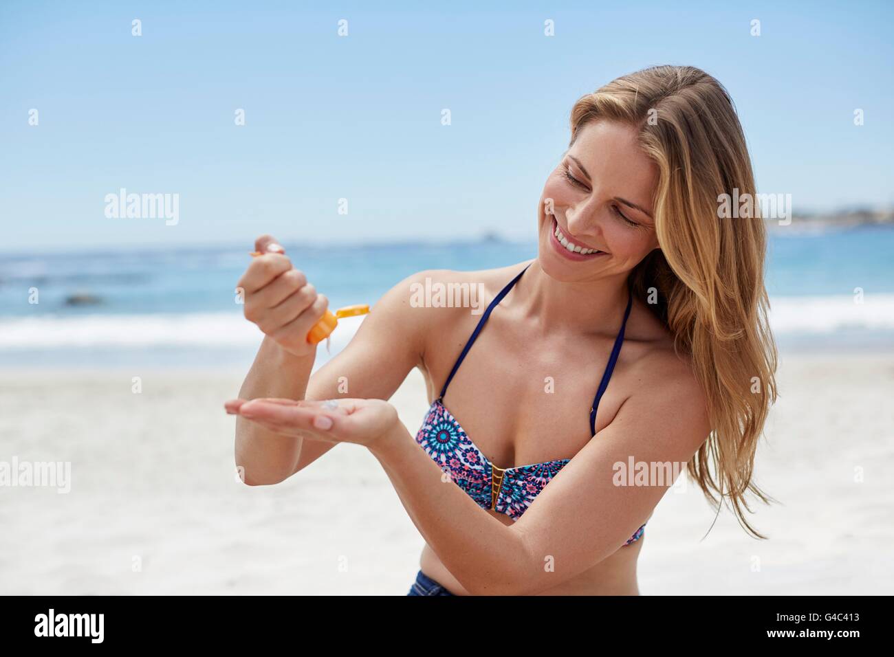 -MODELL VERÖFFENTLICHT. Junge Frau, die Anwendung von Sonnencreme am Strand. Stockfoto