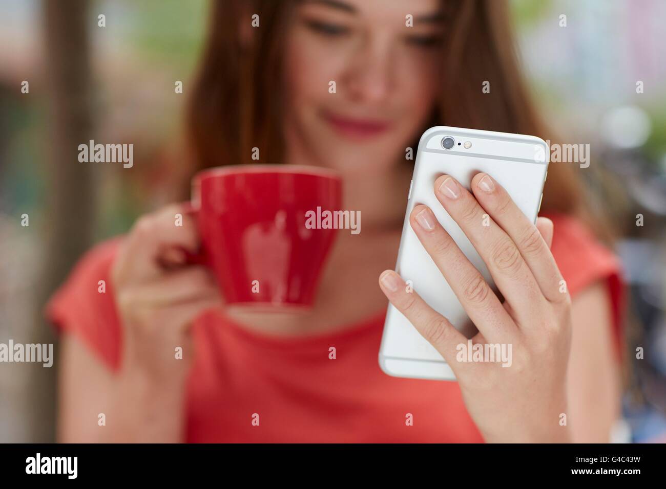 -MODELL VERÖFFENTLICHT. Junge Frau mit Smartphone, Kaffee trinken, Nahaufnahme. Stockfoto