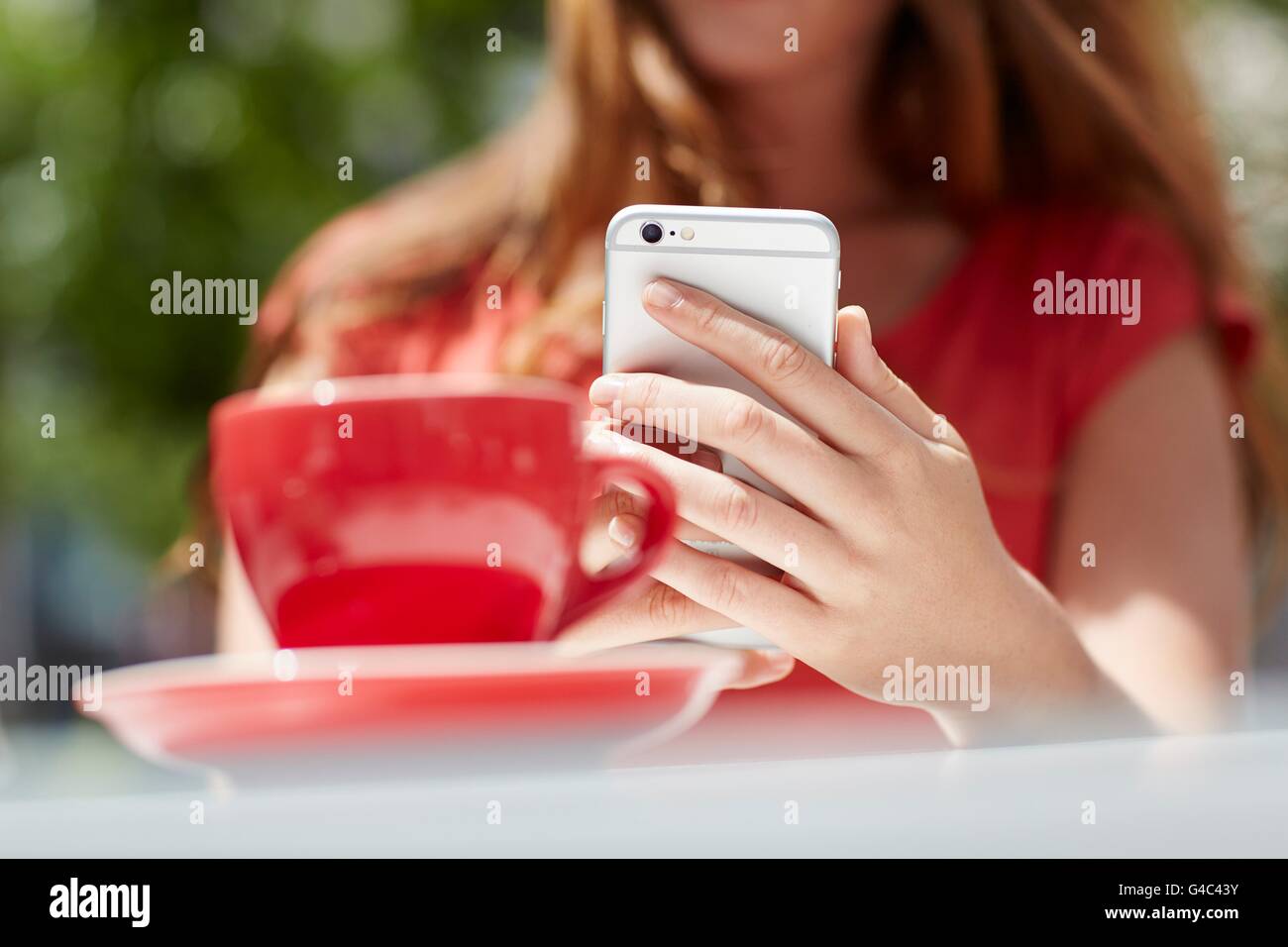 -MODELL VERÖFFENTLICHT. Junge Frau mit Smartphone mit Kaffee, Nahaufnahme. Stockfoto
