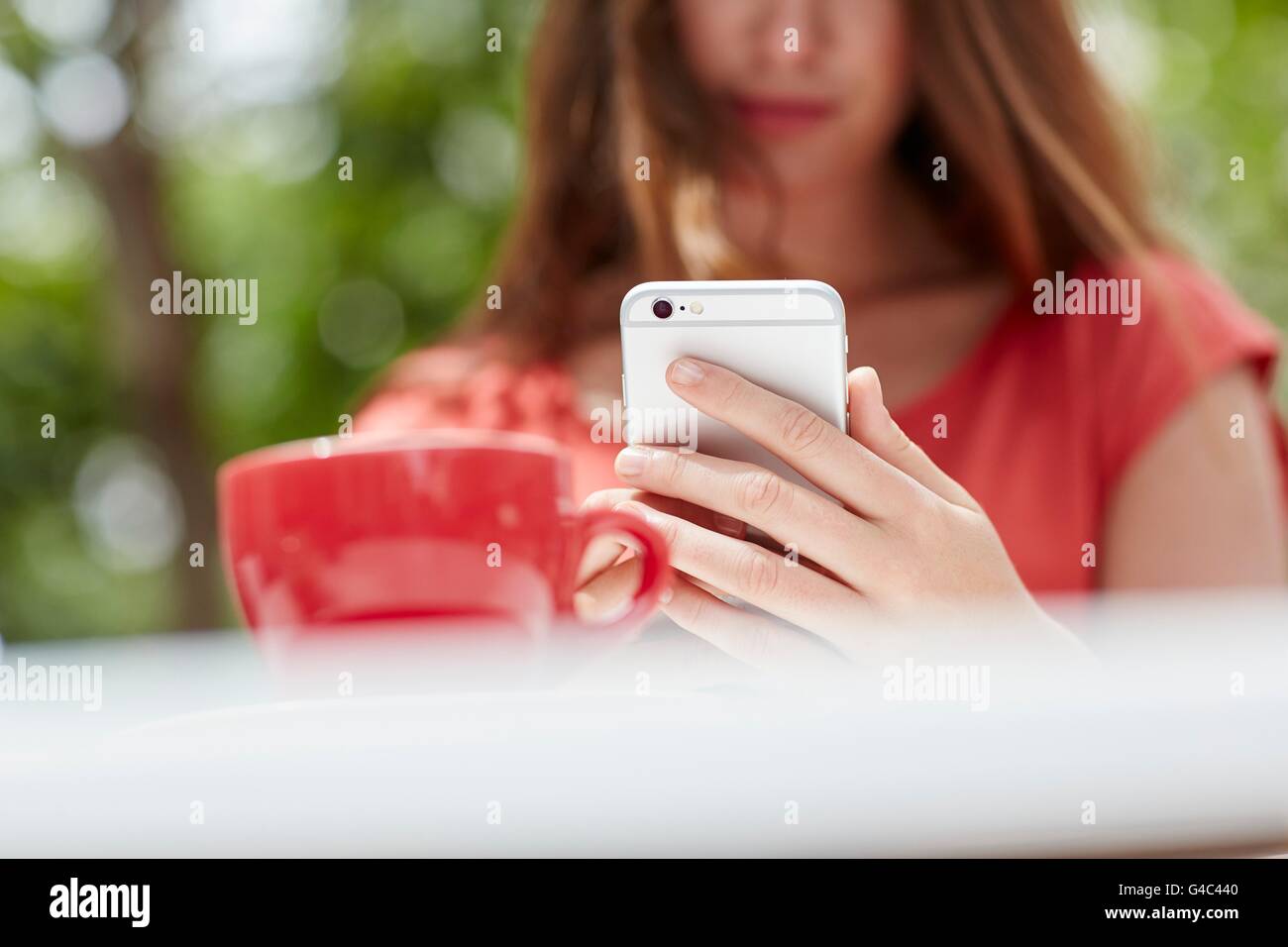 -MODELL VERÖFFENTLICHT. Junge Frau mit Smartphone mit Kaffee, Nahaufnahme. Stockfoto