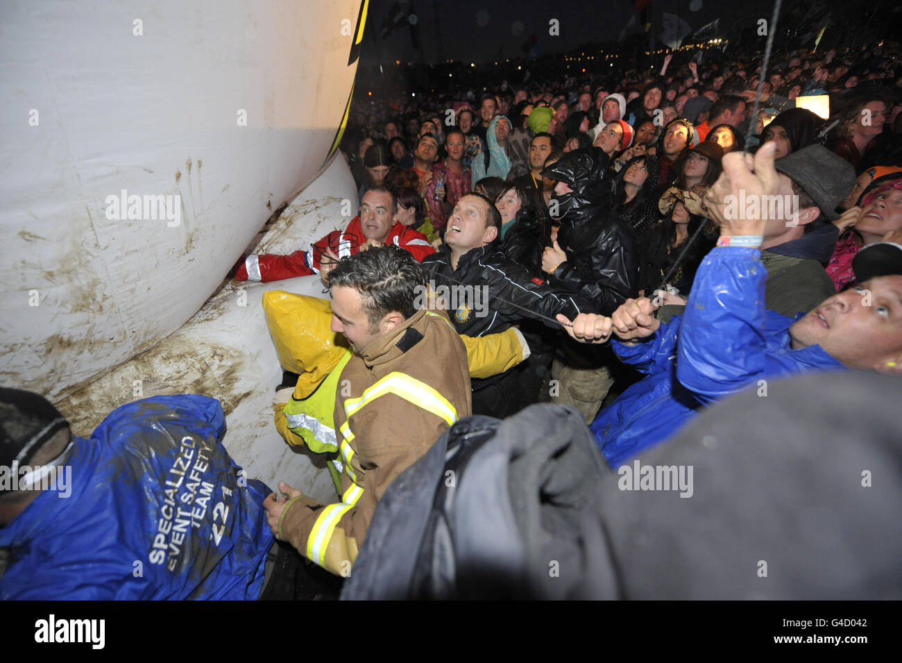 Sicherheitspersonal und Mitglieder der direkten Aktionsgruppe Art Uncut, tossle über einen 20 Fuß großen Ballon mit der Botschaft "U Pay Your Tax 2", während die Rockband U2 auf der Pyramid Stage beim Glastonbury Musikfestival in Worthy Farm, Pilton auftreten. Stockfoto