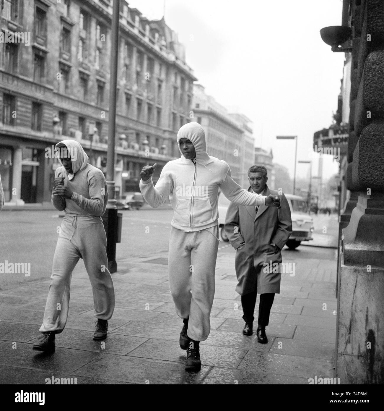 BOXER CASSIUS CLAY, BEGLEITET VON BOXER JIMMY ELLIS (LINKS) WÄHREND EINES FRÜHEN MORGENTRAININGS, JOGGEN ENTLANG DER UNTEREN REGENT STREET, LONDON, ZU SEINEM TRAINING IM HYDE PARK, BEVOR SEIN BRITISCHES SCHWERGEWICHT GEGEN CHAMPION HENRY COOPER ANTRITT Stockfoto