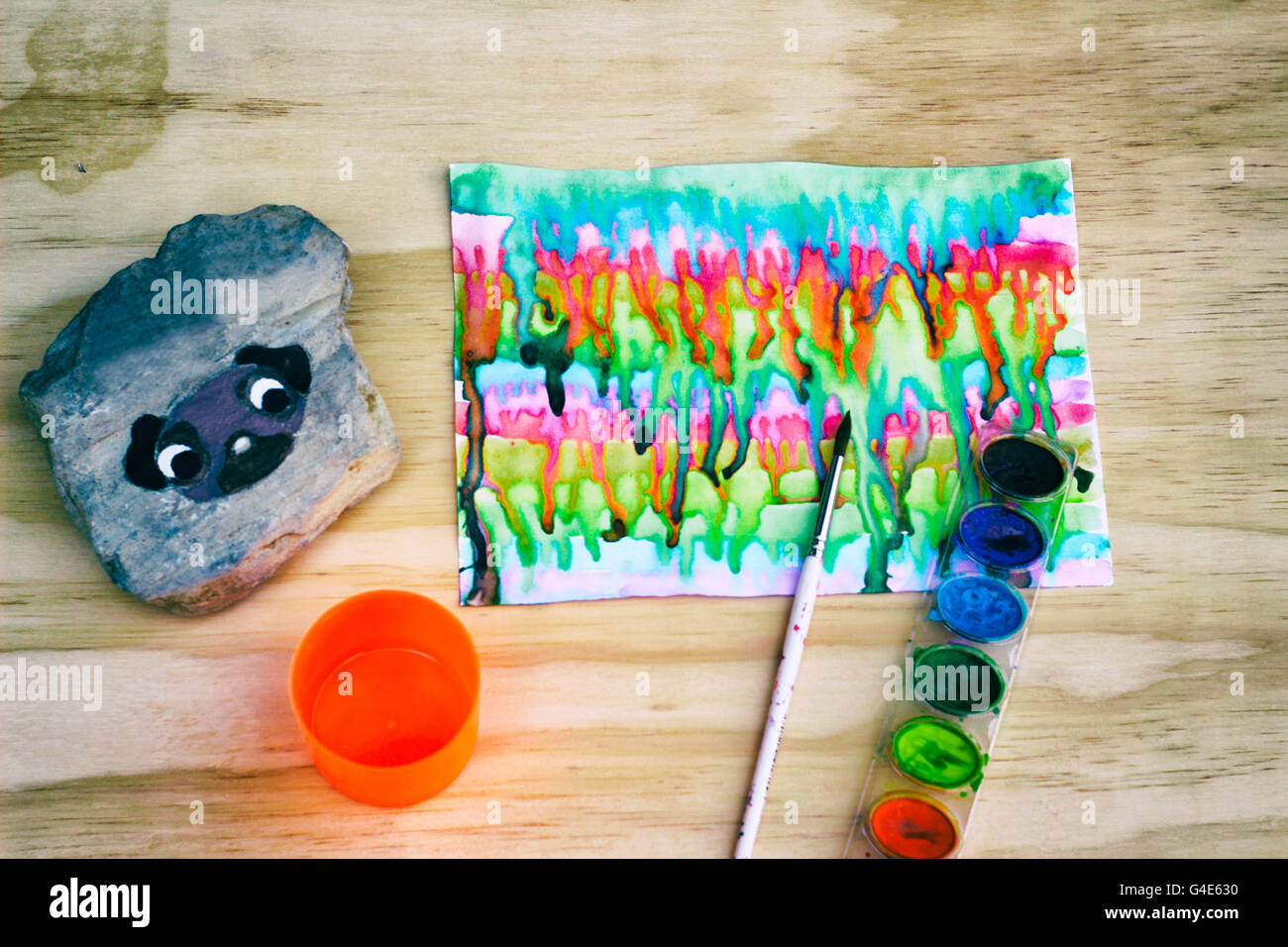 Foto von Aquarellfarbe, einen Pinsel und einen Stein mit einem gemalten Mops Hund drauf auf einem Holztisch Stockfoto