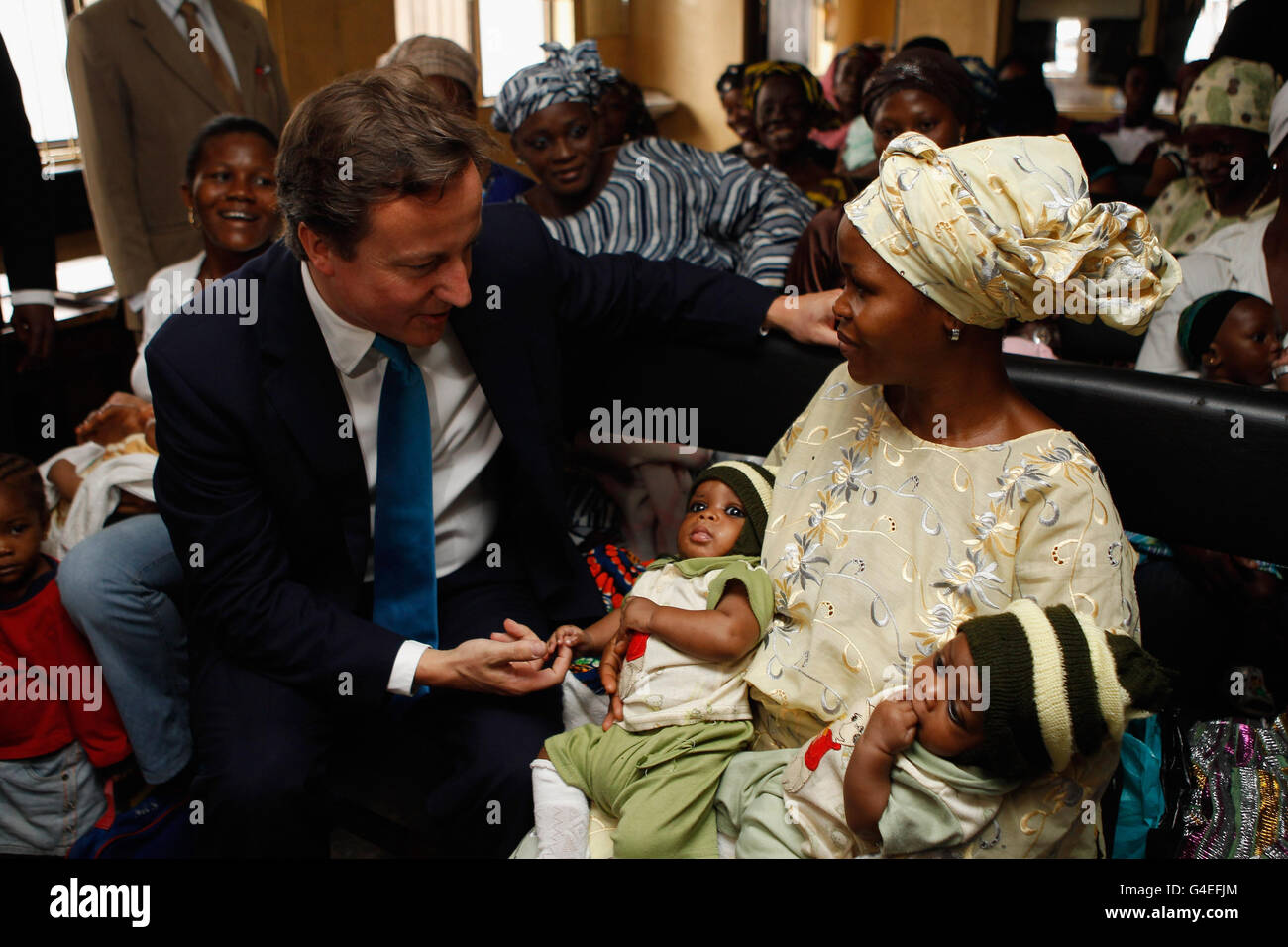 Der britische Premierminister David Cameron plaudert mit einer Mutter (Name unbekannt) und den Zwillingen Mubarak und Mubarakat, während er eine Impfklinik der GAVI Alliance in Lagos, Nigeria, besucht, wo Kinder gegen Gelbfieber geimpft werden, die von der britischen Regierung bezahlt werden. Stockfoto