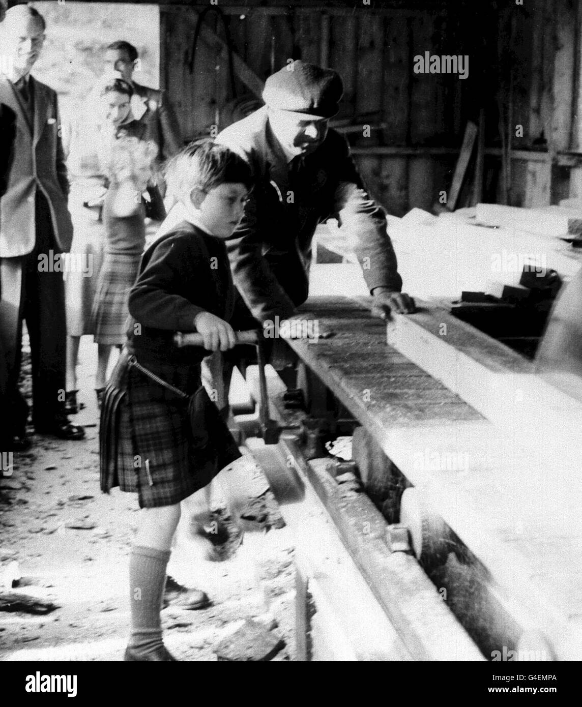 Der achtjährige Prinz Charles versucht sich an der Sägemühle, als die königliche Familie die Forstplantage auf dem Anwesen Balmoral Castle in Balmoral, Aberdeenshire, Schottland besuchte. Der Herzog von Edinburgh, Königin Elizabeth II und Prinzessin Anne beobachten den jungen Prinzen aus dem Hintergrund. Stockfoto