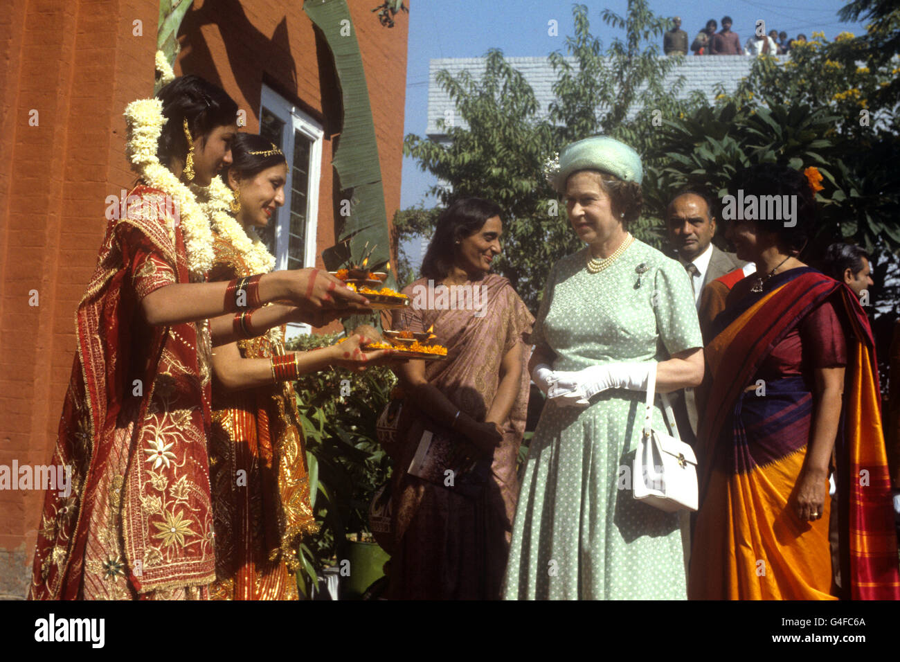Die Königin wird Essen von Mädchen in traditionellen indischen Kleid an der Mahatma Gandhi Denkmal in Raj Ghat, Delhi angeboten. Gandhi wurde hier nach seiner Ermordung eingeäschert. Dies war der zweite Besuch der Königin auf der Website, die erste war im Jahr 1961, als sie einen Baum gepflanzt. Stockfoto