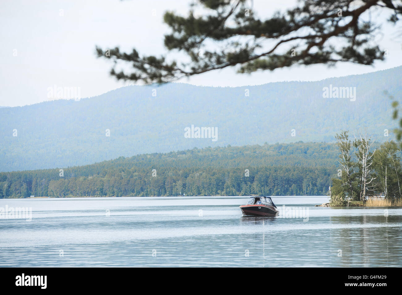 Motor Boot schwimmt auf dem Wasser des Sees, umgeben von Bergen und Wäldern Stockfoto