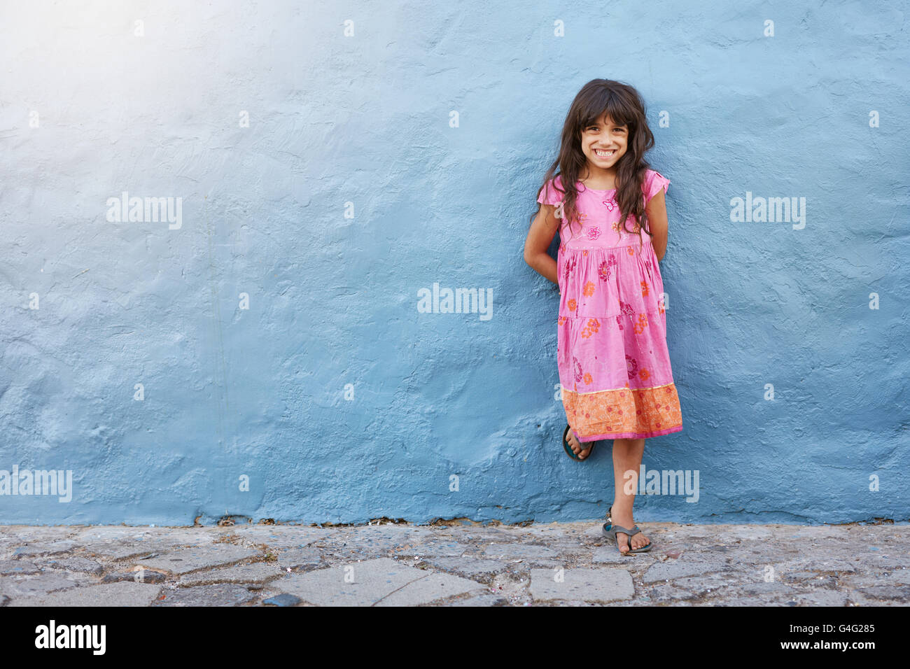 In voller Länge Portrait von niedliche kleine Mädchen lächelnd stehend gegen blaue Wand mit Textfreiraum Stockfoto