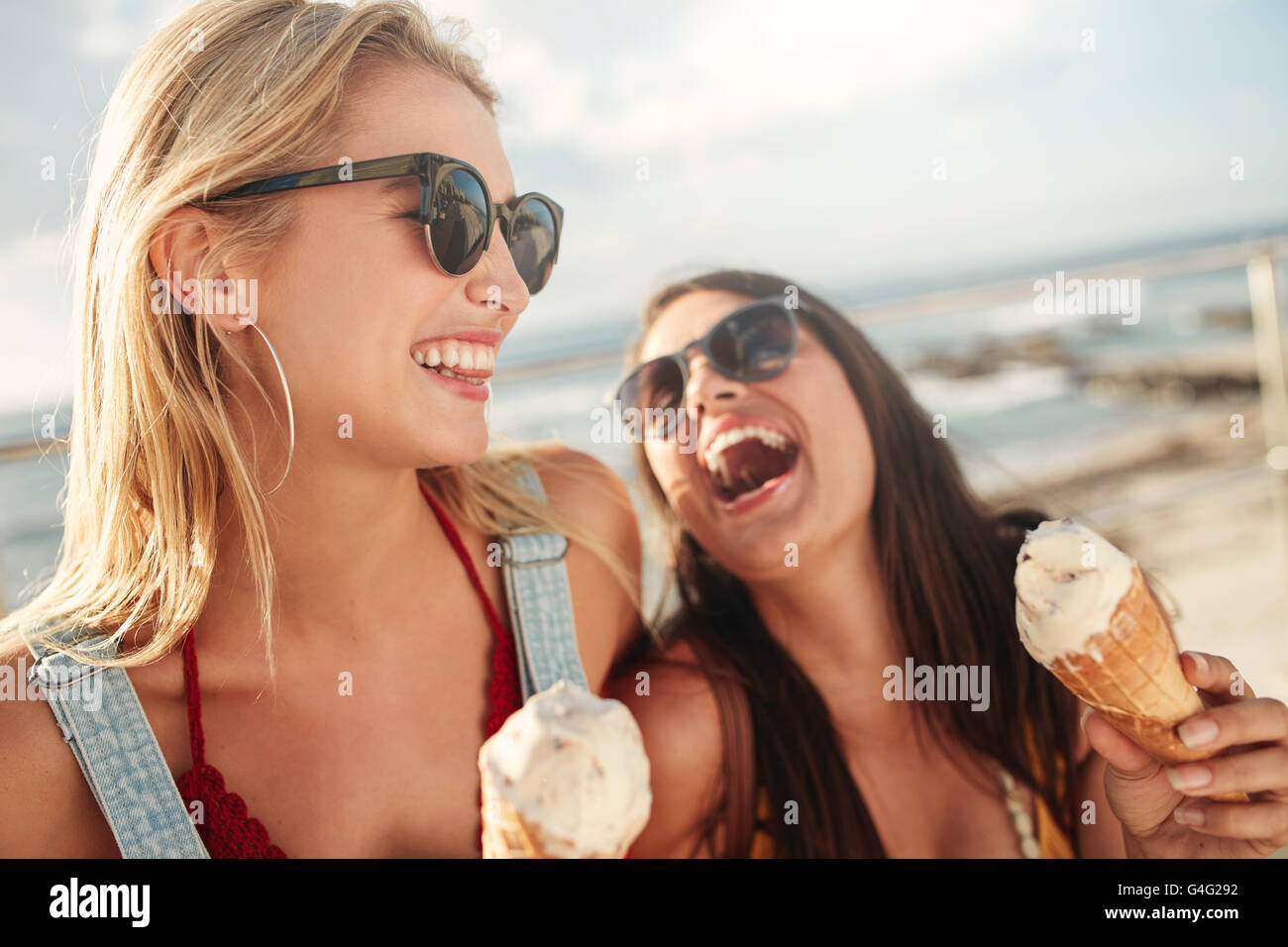 Zwei junge Frauen stehen, zusammen lachen und essen Eis. Glückliche junge Freundinnen mit Eis genießen gemeinsam auf eine Stockfoto