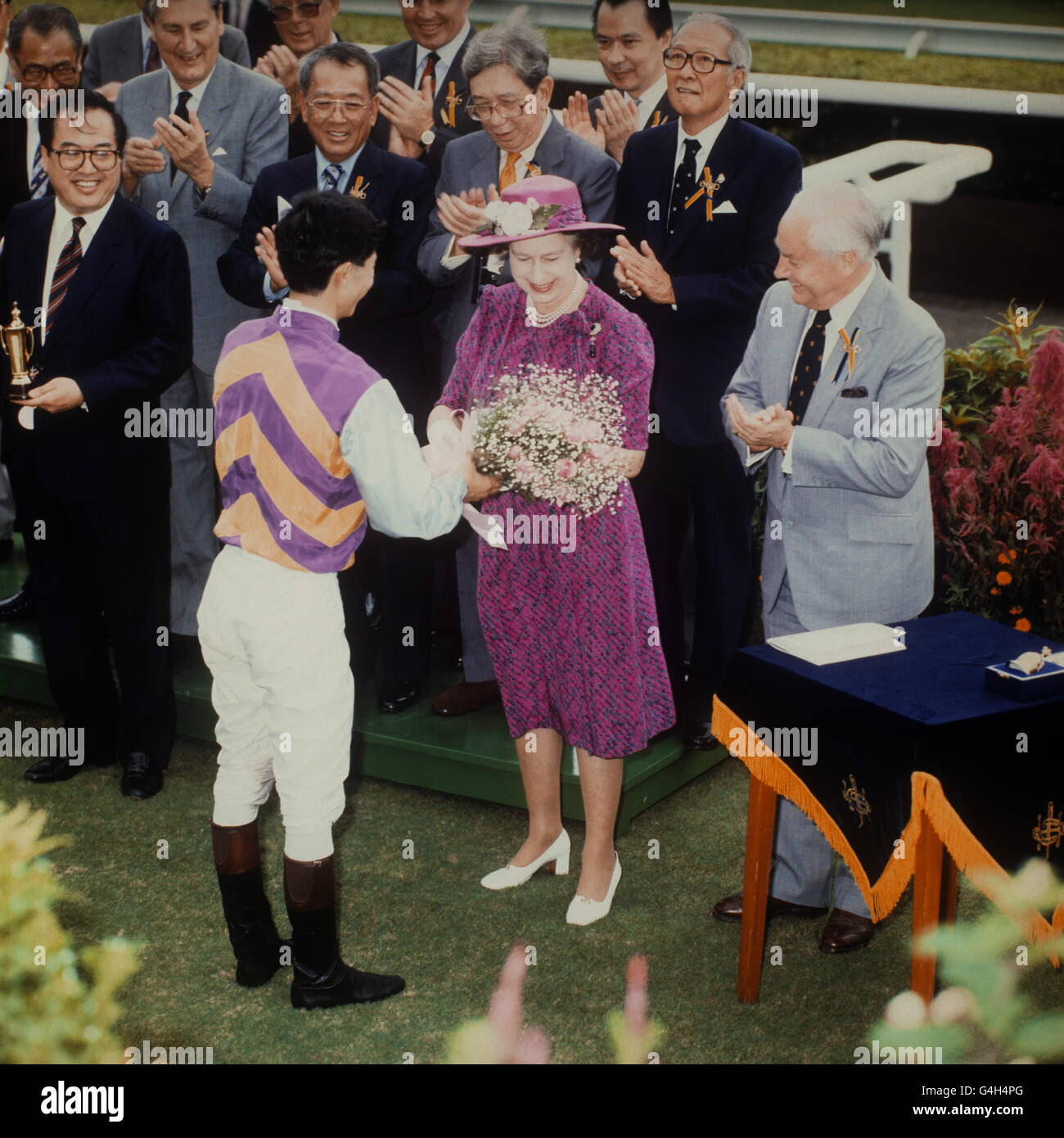 Die Königin präsentiert dem siegreichen Jockey einen Blumenstrauß, nachdem er auf dem Sha Tin-Kurs „Forever Gold“ zum Sieg geritten hatte, wo die Königin Gast des Royal Hong Kong Jockey Club war. Stockfoto