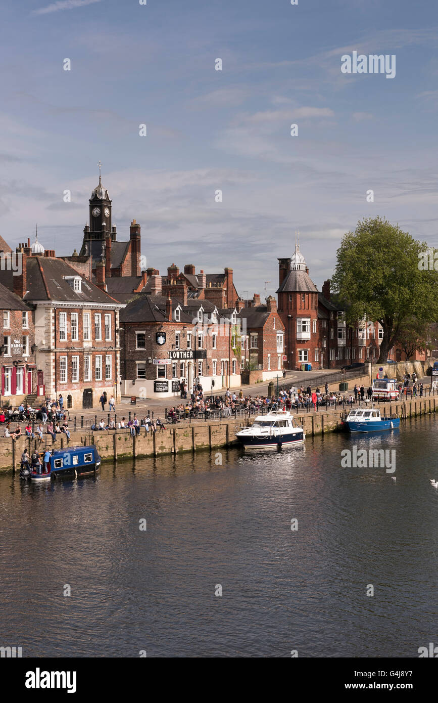 Viele Leute trinken und entspannen in der Sonne in geschäftigen Pubs am Flussufer und Freizeitboote, die auf dem Fluss Ouse - King's Staith, York, North Yorkshire, England - festgemacht sind. Stockfoto