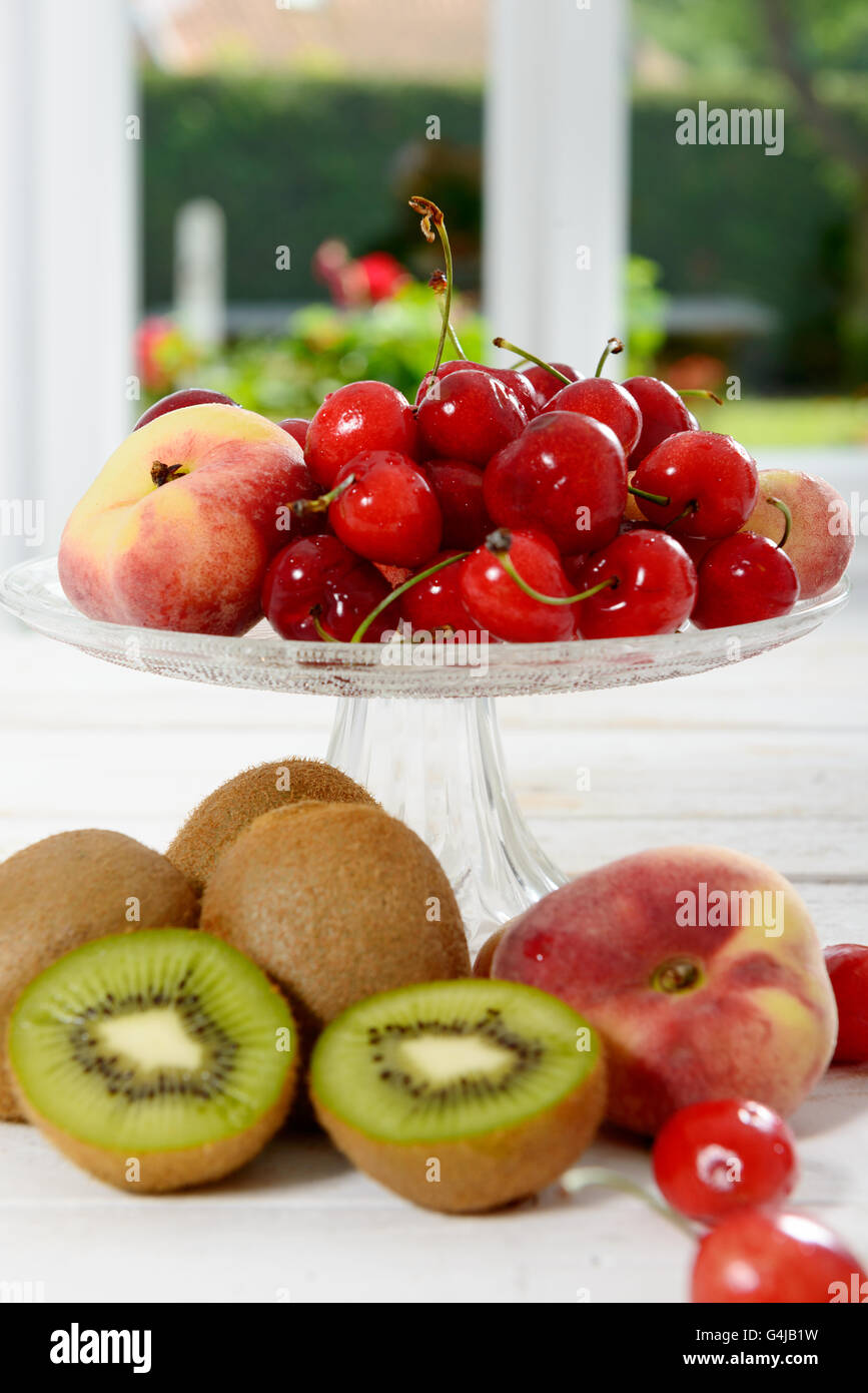 einige Kirschen, Kiwis und Pfirsiche in eine Glasschale Stockfoto