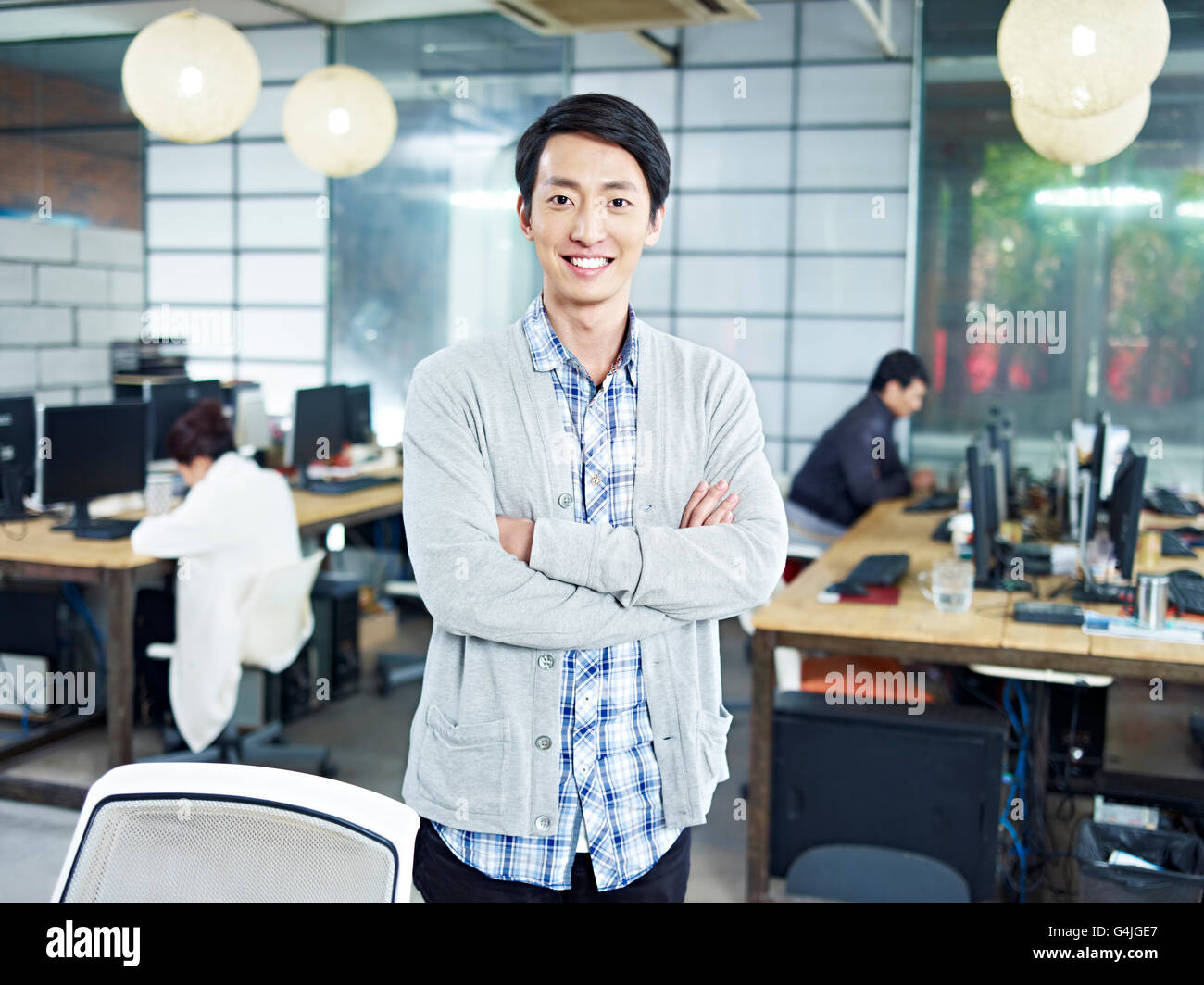 zuversichtlich jungen asiatischen Unternehmer im eigenen Unternehmen betrachten Kamera verschränkten Armen lächelnd stehen. Stockfoto