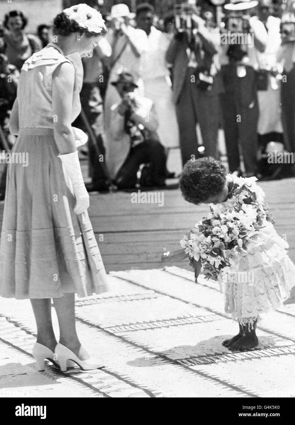 Die Königin lächelt auf Mei Kainona herab, während sich das vierjährige Fidschi-Mädchen tief verbeugt, bevor es ihr in Suva einen Blumenstrauß mit einheimischen Blumen übergibt. Stockfoto