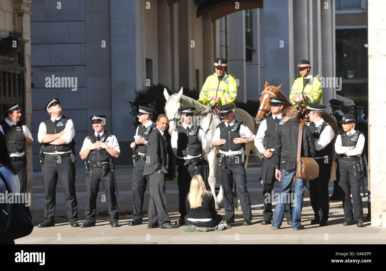 Eine Frau sitzt an der Polizeilinie am Paternoster Square in London, da Offiziere einen Protest gegen das globale Finanzsystem enthalten. Stockfoto