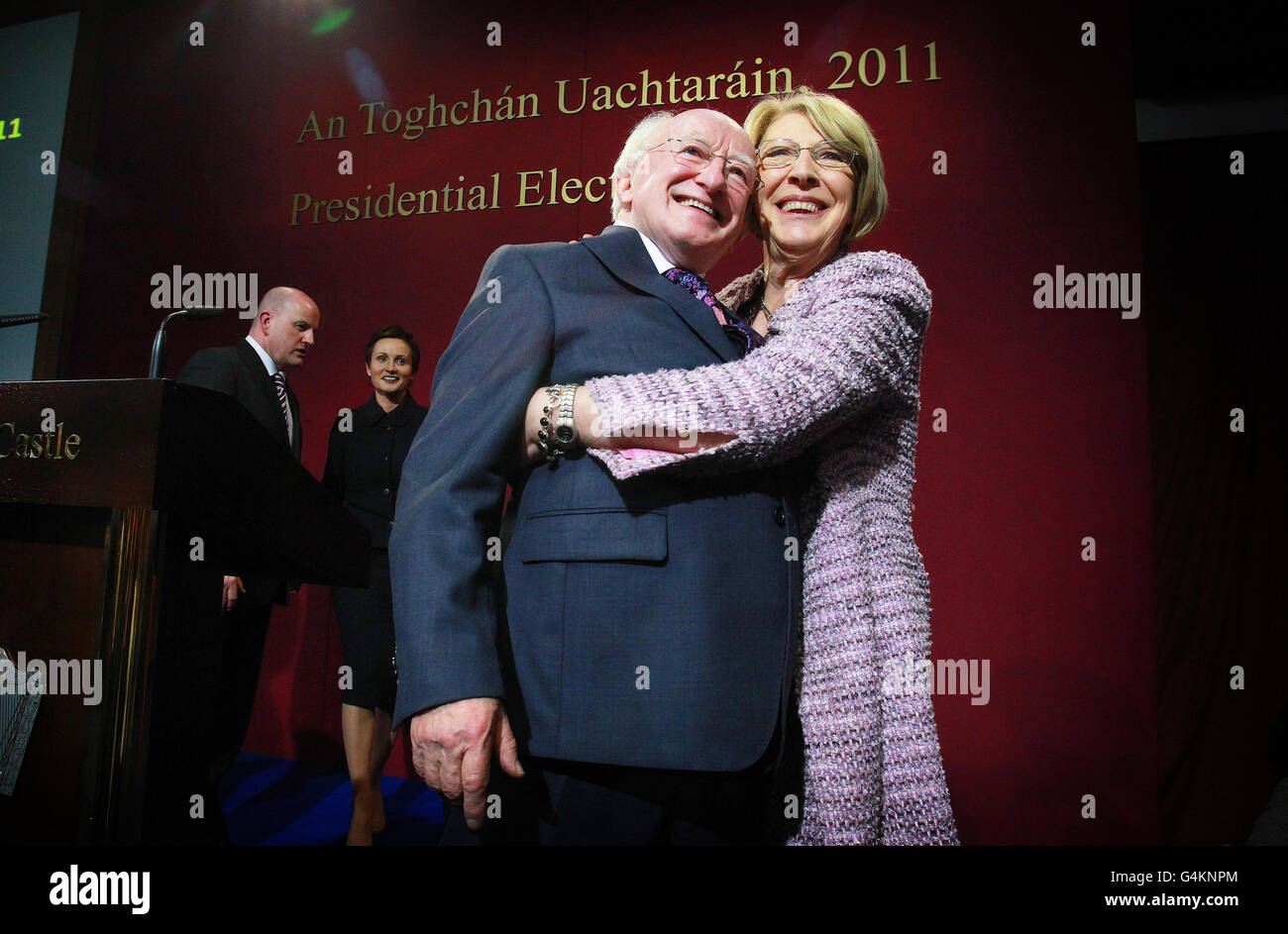 Labour-Kandidat Michael D Higgins wird von seiner Frau Sabina Coyne umarmt, als der besiegte Kandidat Sean Gallagher und seine Frau Trish Gallagher die Ankündigung der ersten Vorzugsstimmen bei der irischen Präsidentschaftswahl im Count Center in Dublin Castle betrachten. Stockfoto