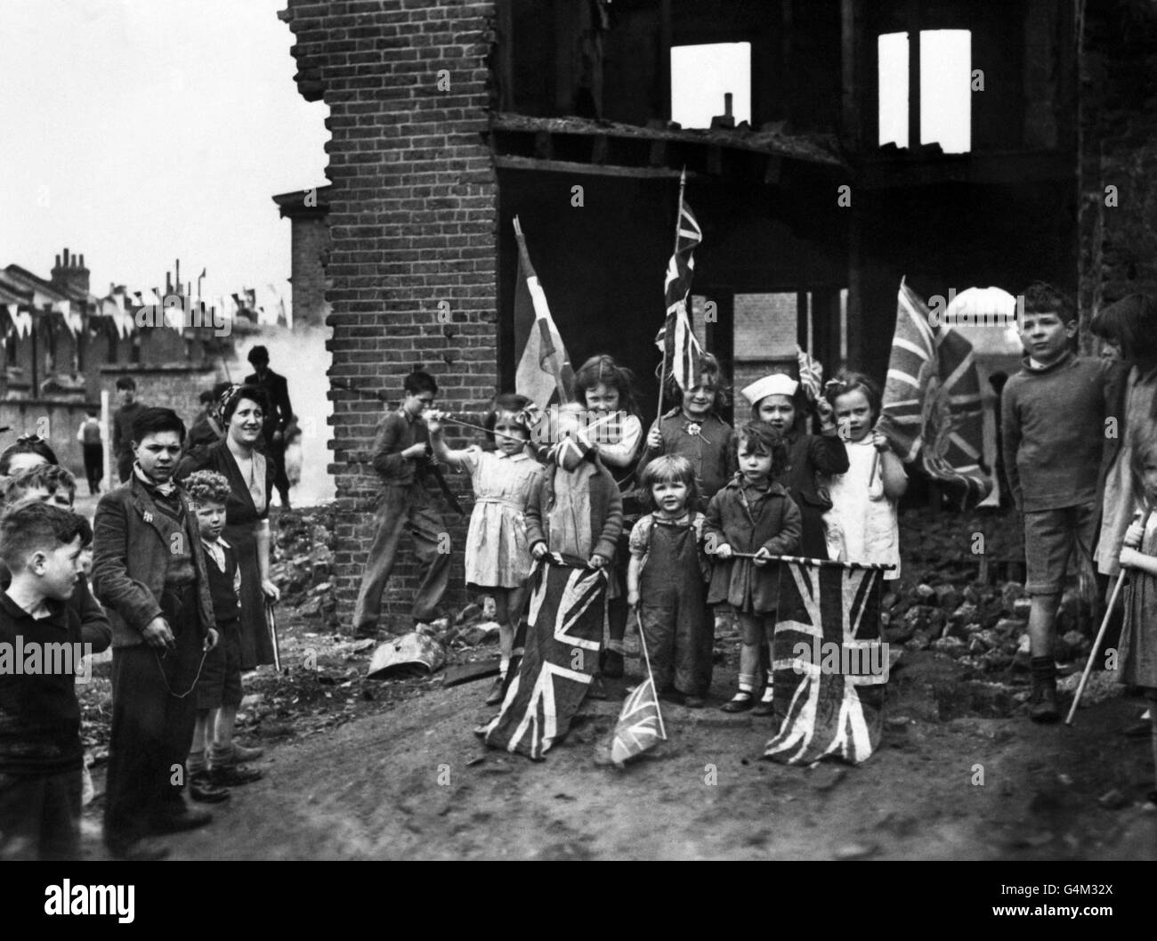 Junge Londoner feiern den VE-Day (Victory-in-Europe Day), der das Ende des Krieges in Europa markiert, inmitten der Ruinen ihres Hauses in Battersea. Stockfoto