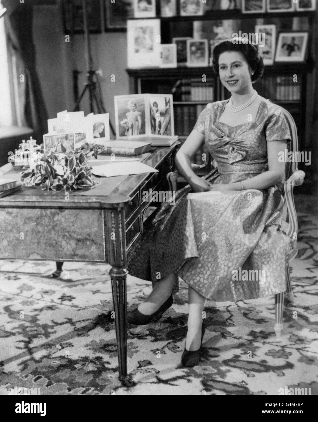 Die Königin, in einem goldgelähmten Kleid, wird in der Long Library in Sandringham kurz nach der Übertragung des traditionellen Weihnachtstages an ihre Völker gesehen. Auf dem Schreibtisch befinden sich Porträts von Prinz Charles und Prinzessin Anne. Die Sendung wurde zum ersten Mal im Fernsehen übertragen und sowohl von der BBC als auch von ITV übertragen. Es war der 25. Jahrestag der ersten Radiobotschaft ihres Großvaters, König George V. an den Commonwealth Stockfoto