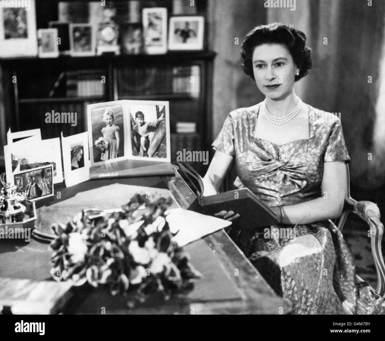 Die Königin, in einem Gold lahmen Kleid, wird in der Long Library in Sandringham kurz nach der Herstellung der traditionellen Weihnachtstag Sendung an die Nation gesehen. Auf dem Schreibtisch befinden sich Porträts von Prinz Charles und Prinzessin Anne. Die Königin hält die Kopie von "Pilgrim's Progress", aus der sie während ihrer Botschaft einige Zeilen las. Die Sendung wurde in diesem Jahr zum ersten Mal im Fernsehen übertragen und sowohl von der BBC als auch von ITV übertragen. Es war der 25. Jahrestag der ersten Radiobotschaft an den Commonwealth von ihrem Großvater, König George V. Stockfoto