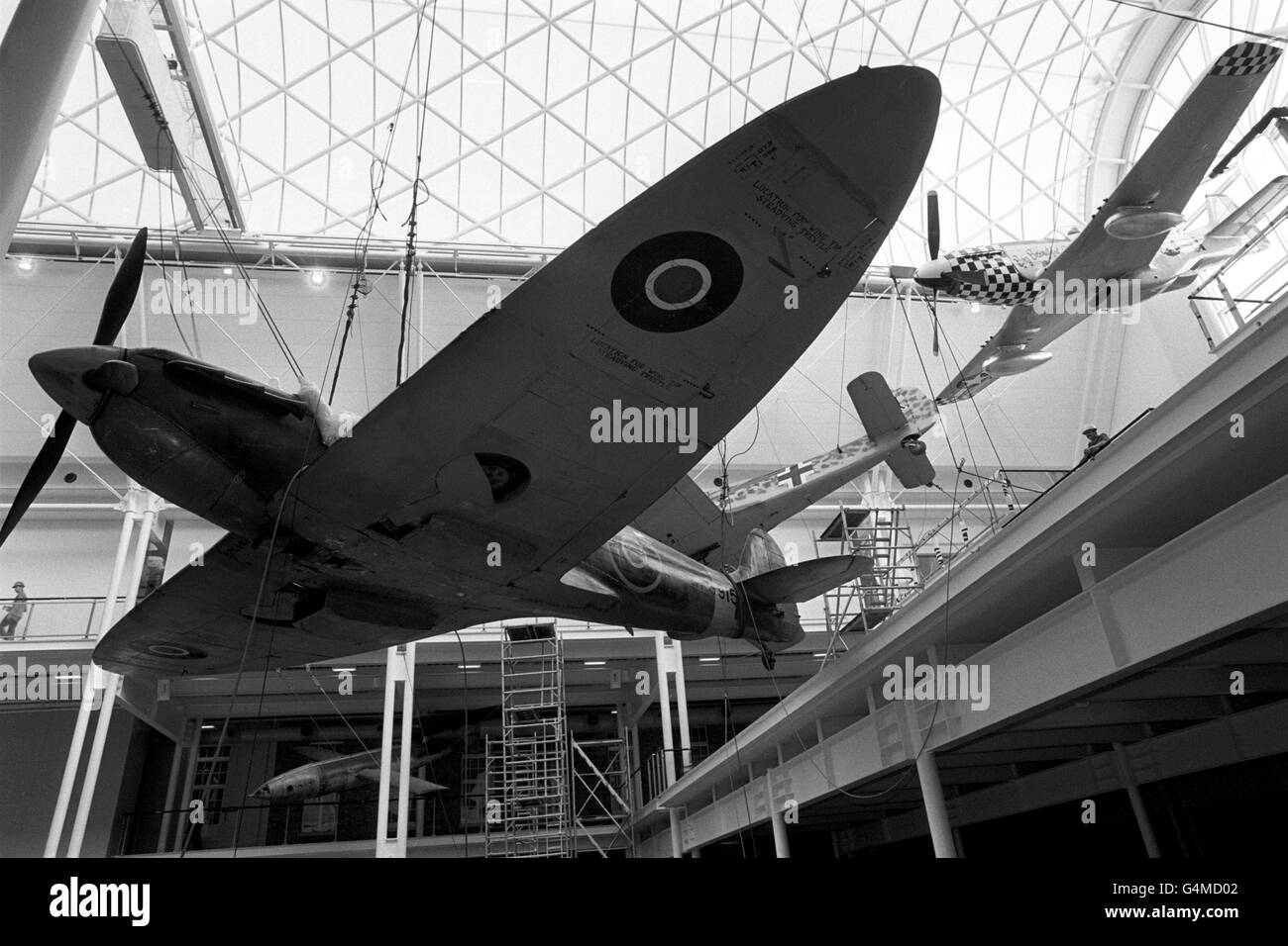 Die Battle of Britain Spitfire des Imperial war Museum ist 50 Meter hoch in der neuen Hauptausstellungshalle in London aufgehängt. Es ist das Herzstück der neuen Ausstellung nach großen Umbauarbeiten des Museums. Dahinter steht eine amerikanische P51 Mustang (r) und eine deutsche Focke Wulf 190 Stockfoto