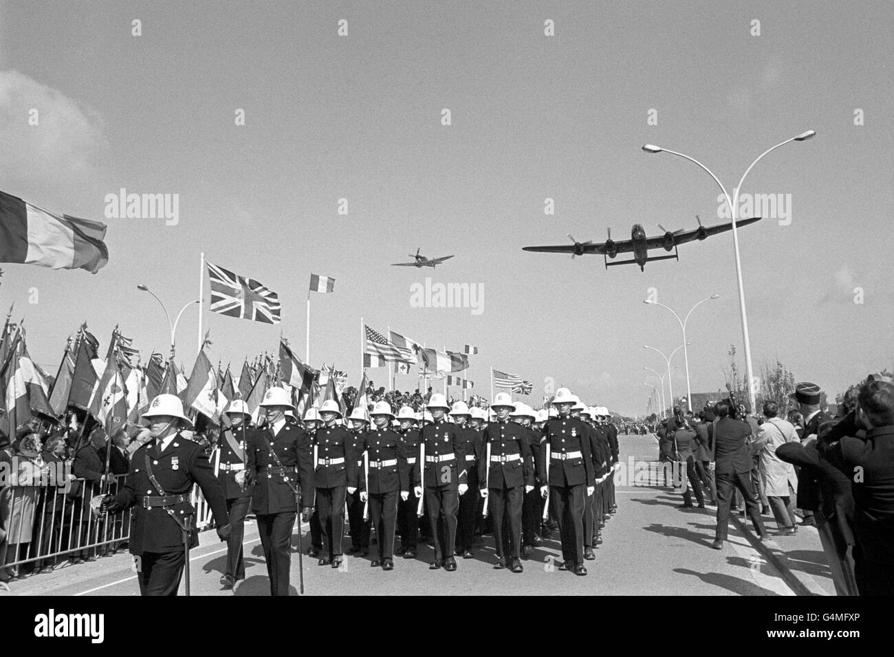 Ein Spitfire-Kämpfer der Royal Air Force und ein Lancaster-Bomber fliegen über die Feierlichkeiten zum 25. Jahrestag der Landung der Normandie im Zweiten Weltkrieg in Frankreich. Hier marschieren eine Parade der Royal Marines vorbei Stockfoto
