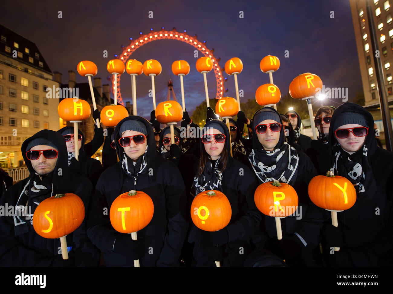 Geheimnisvolle schwarze Figuren, die mit geschnitzten Kürbissen bewaffnet sind, posieren an Halloween neben dem Londoner Auge, um die neue Show 'American Horror Story' auf dem britischen FX-Kanal zu starten. Stockfoto