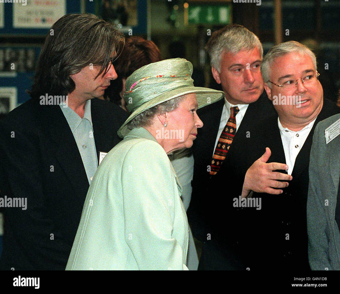 Königin Elizabeth II., die vom Duke of Edinburgh begleitet wurde, hält an, um mit Michael starke zu plaudern, der Sinbad (R) aus der TV-Seife "Brookside" und dem Serienschöpfer Phil Redmond (L) in der Liverpool Central Library spielt. Stockfoto