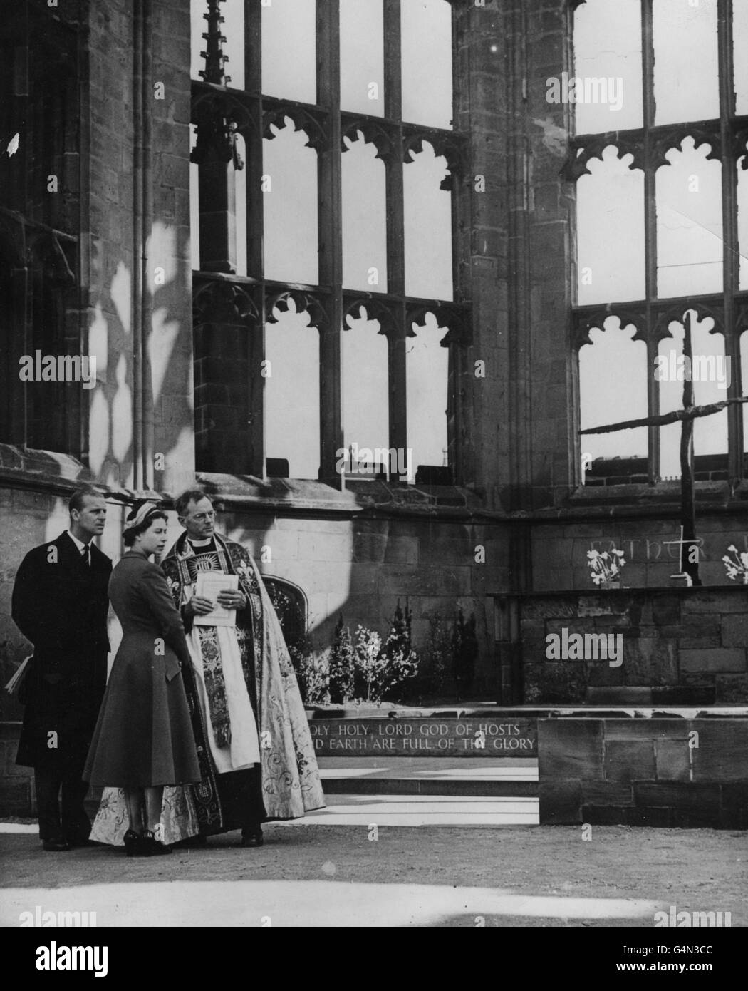 Königin Elizabeth II. Und der Herzog von Edinburgh mit dem Provost von Coventry, dem Very Rev. R.T Howard, im Sanctuary der alten Coventry Cathedral. Sie sehen das verkohlte Kreuz, das aus Balken auf dem Dach des Doms besteht, nachdem es in der Nacht vom 14. November 1940 von deutschen Bombern zerstört wurde. Stockfoto