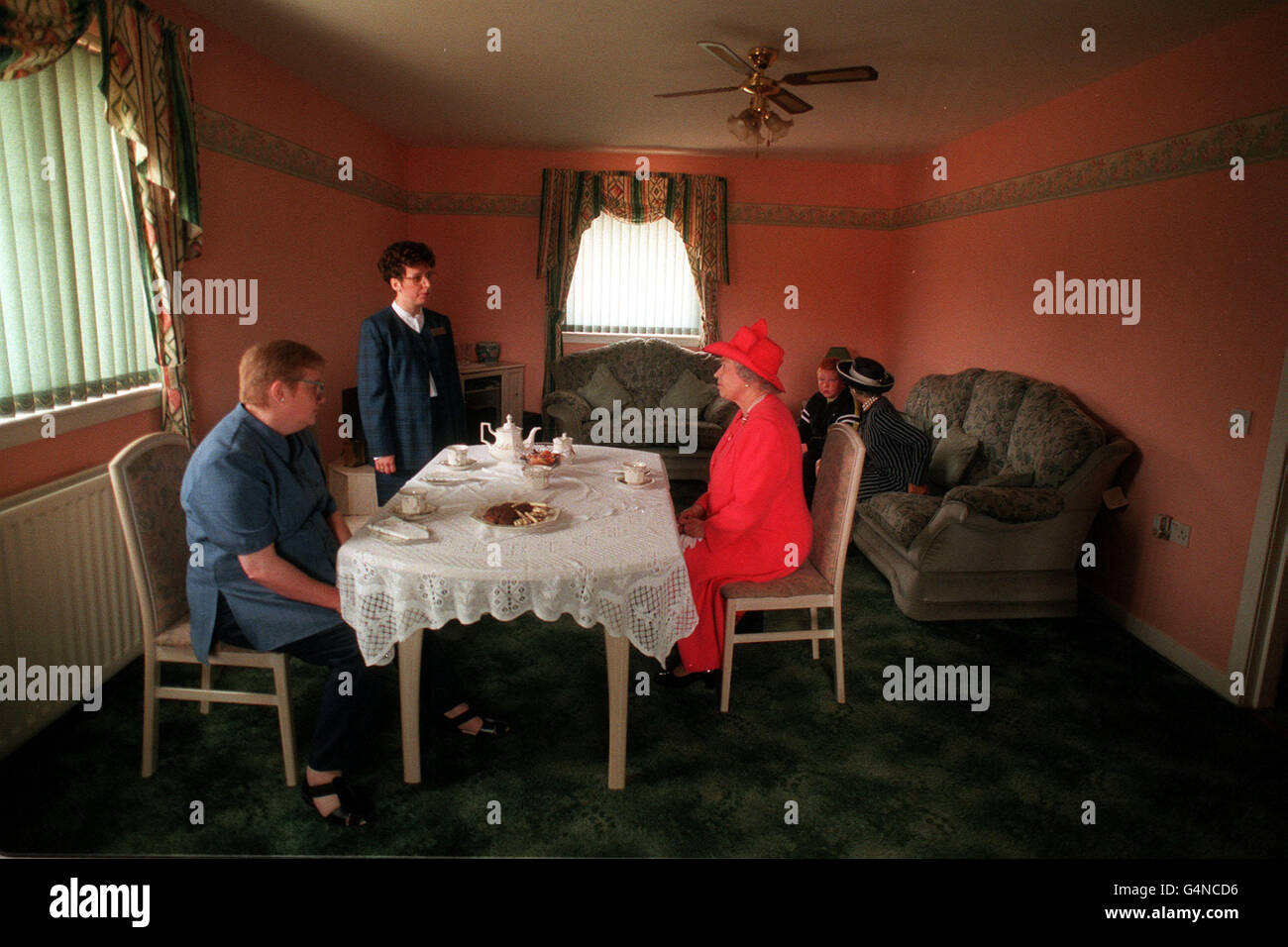 Die Queen kam zu Frau Susan McCarron (vorne links), ihrem zehn Jahre alten Sohn James und der Housing Manager Liz McGuinnis zum Tee in ihrem Haus im Castlemilk-Viertel von Glasgow. 12/4/04: In der neuesten Ausgabe des DK Eyewitness Travel Guide to Great Britain heißt es, dass der Nachmittagstee in britischen Häusern nach wie vor eine Tradition ist, die in diesem Sommer "täglich umgesetzt" wird, und rät Besuchern, "Platz für ein Stück Obstkuchen oder Marmeladenschwamm zu lassen". Stockfoto