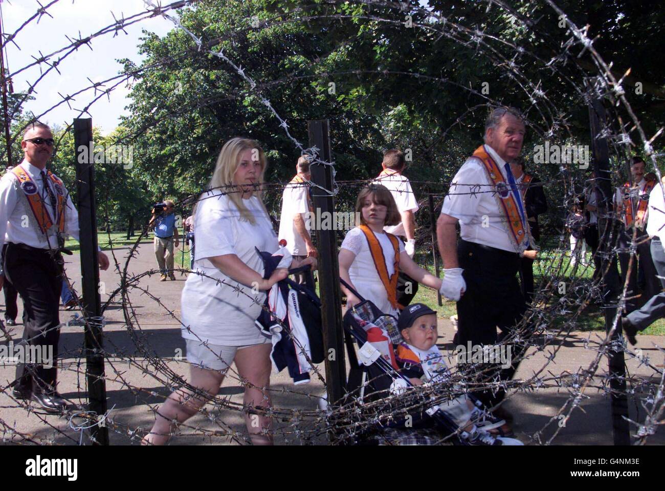 Orangemen und ihre Familien gehen durch eine Lücke in Stacheldraht zum Ormeau Park in Belfast. Die traditionelle Route der Zwölften Juliparade von Ballynafeigh Orangemen wurde von der Paraden-Kommission verboten.die Hauptparade von Belfast fand dann im Ormeau Park statt. Stockfoto