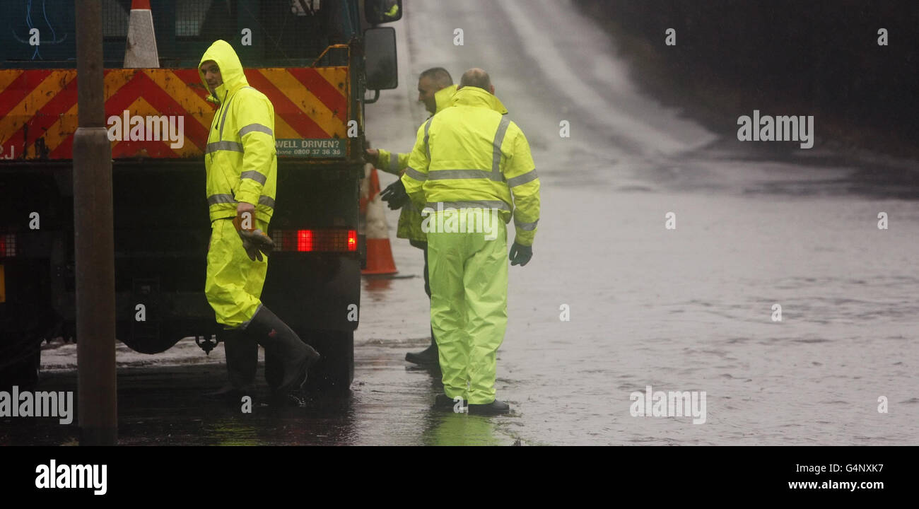 Die Mitarbeiter des Rates sind neben einem überfluteten Abschnitt der Balmore Road in der Nähe von Glasgow abgebildet. Stockfoto