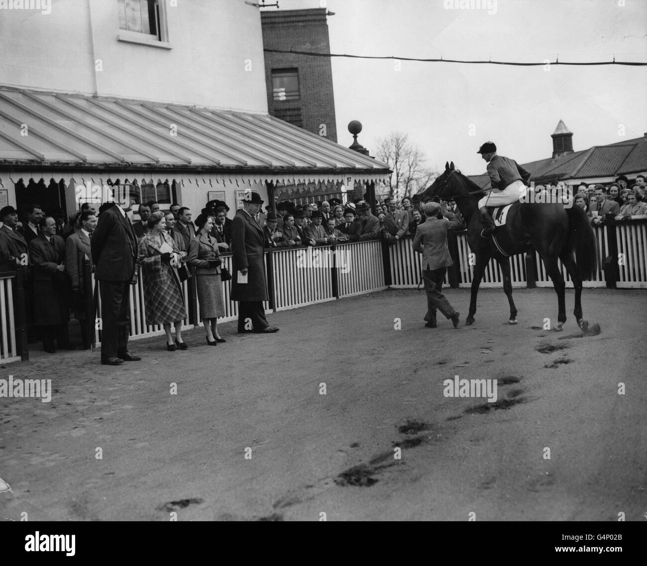 Königin Elizabeth II. Und Prinzessin Margaret beobachten, wie der Jockey Harry Carr das Pferd der Königin, Alexander, in die unsättelnde Einzäunung bringt, nachdem er ihn zum Victory Inn der Guineas Trial Stakes 2,000 im Kempton Park gefahren ist. Stockfoto